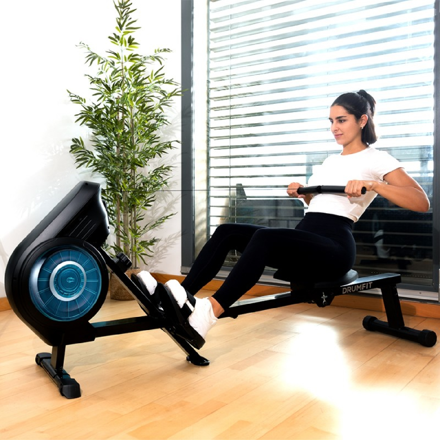 Una mujer con ropa deportiva hace ejercicio en una máquina de remo negra en una habitación luminosa.