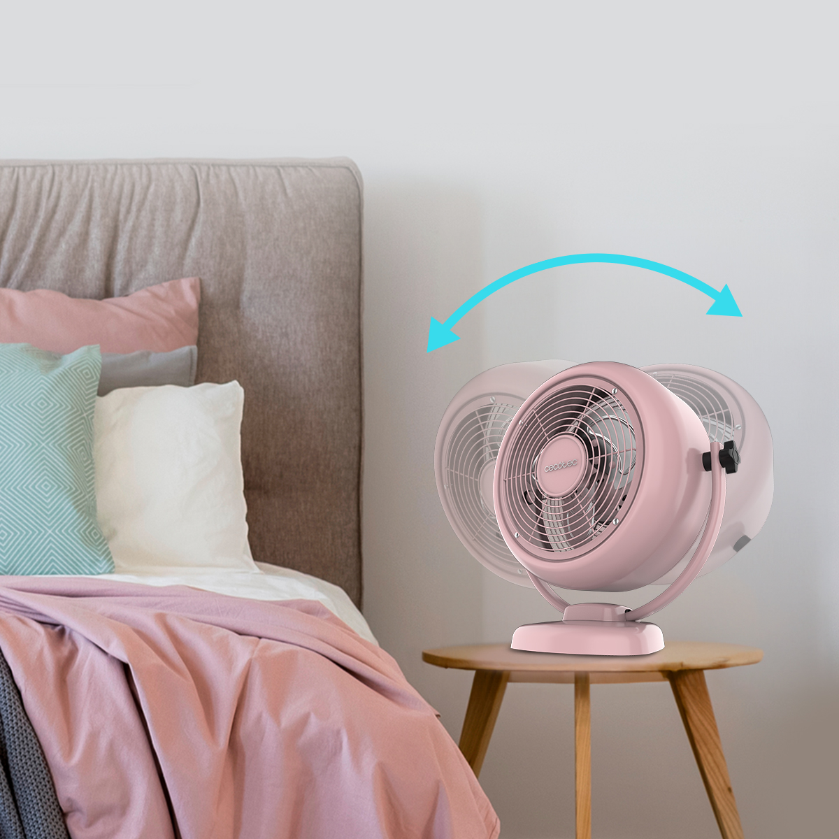 Un ventilatore da tavolo rosa oscilla su un piccolo tavolo di legno vicino a un letto.