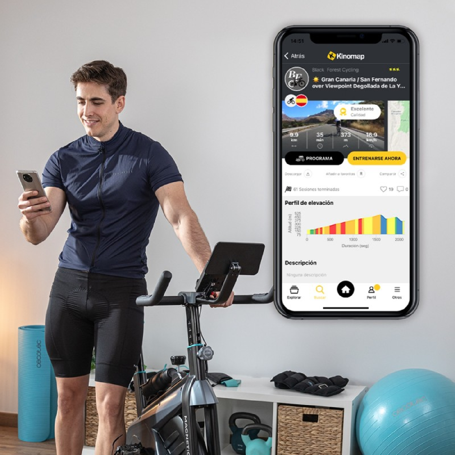 Ciclista junto a bicicleta estática sostiene móvil con app Kinomap.