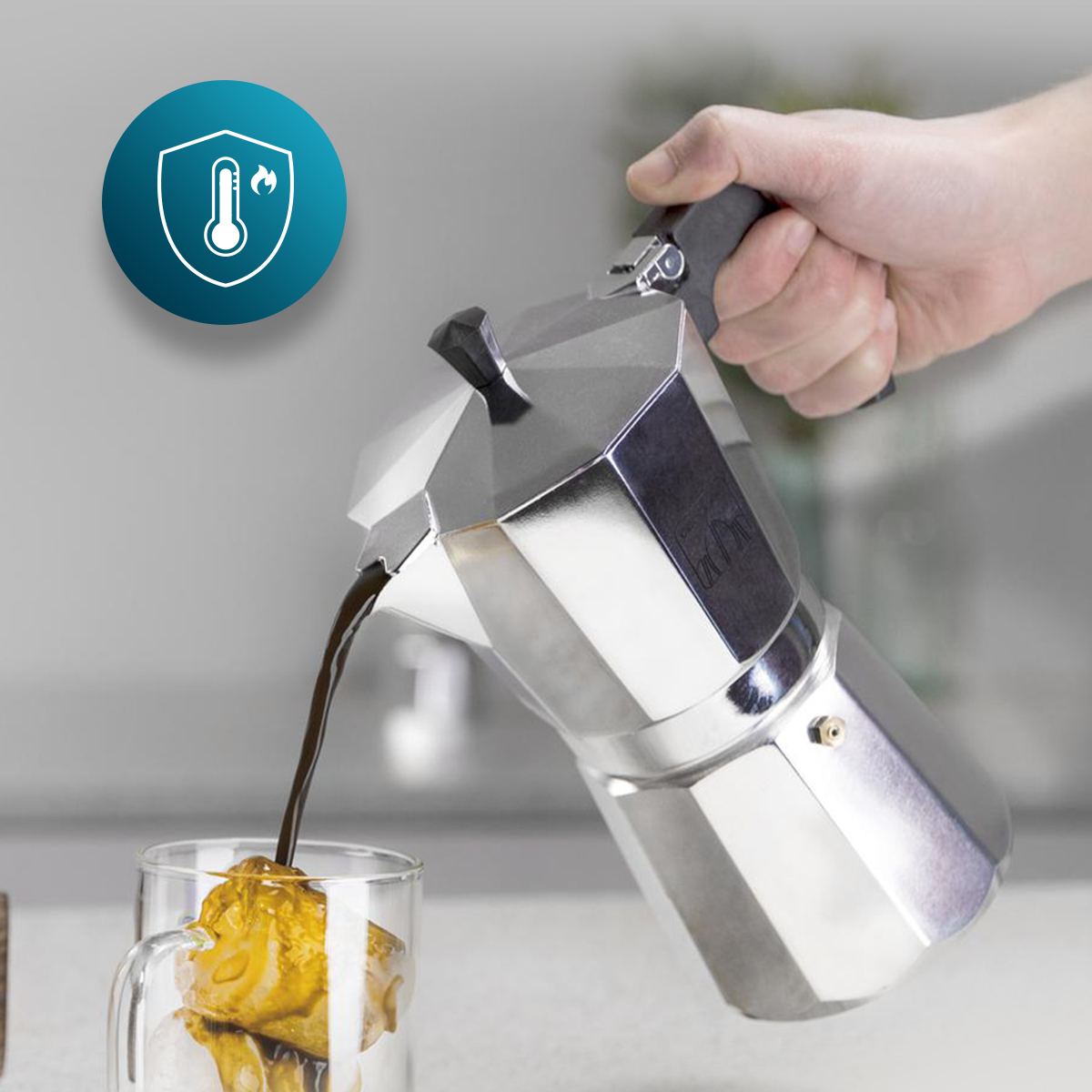 Eine Hand gießt Kaffee aus einer Espressokanne in ein Glas mit Eis. Eine blaue Schutzmarke mit Thermometer ist in der Ecke.