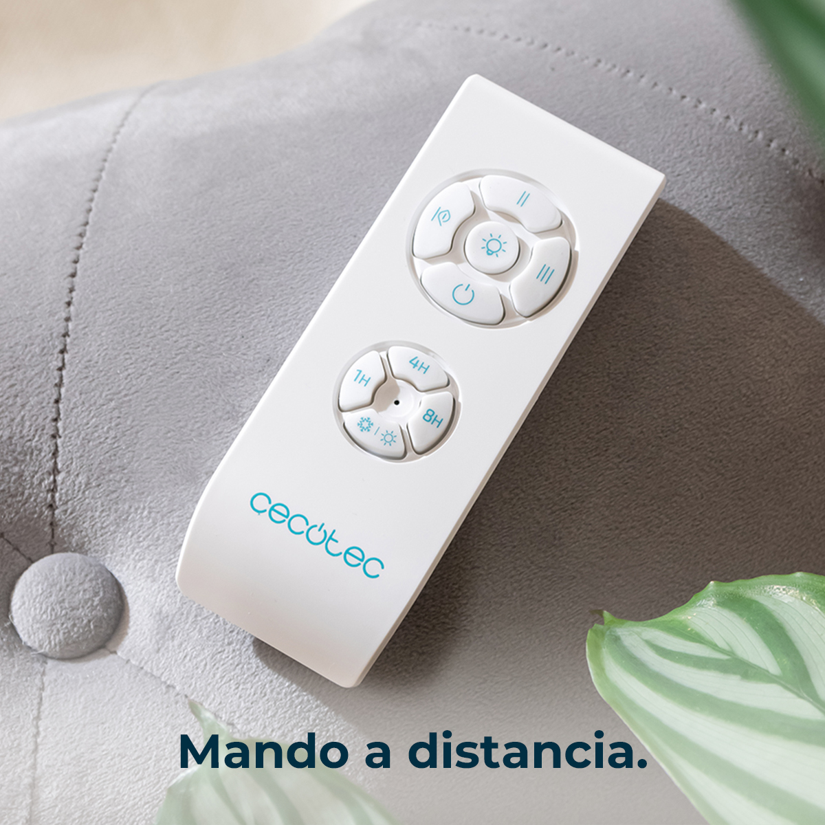 Un mando a distancia blanco de Cecotec sobre una superficie gris con hojas.