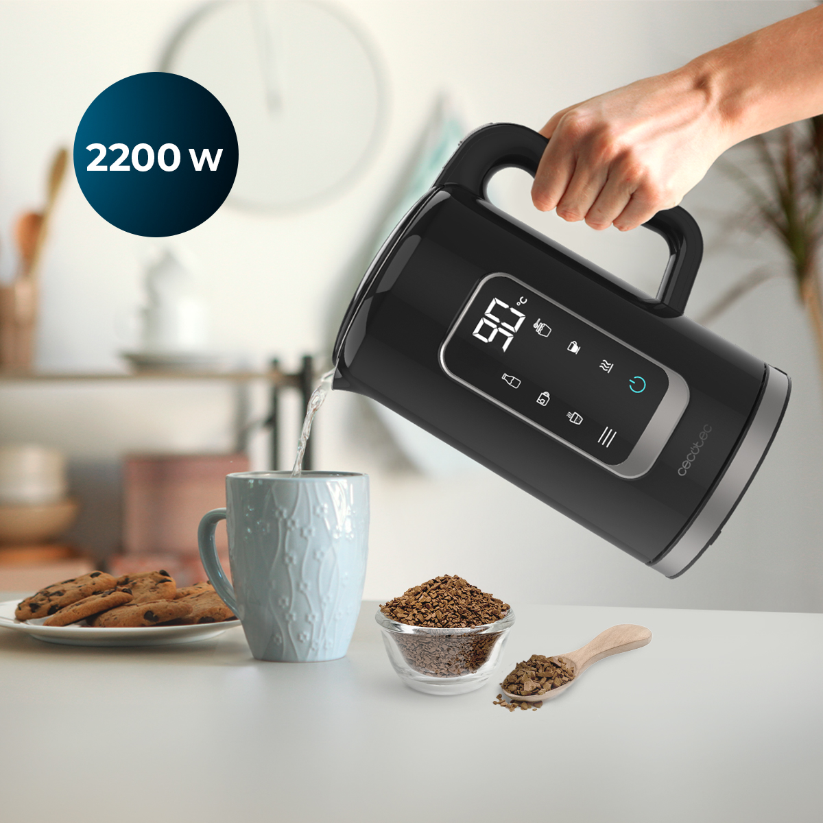 Una mano vierte agua de un hervidor eléctrico negro en una taza azul. Galletas y café en la mesa.