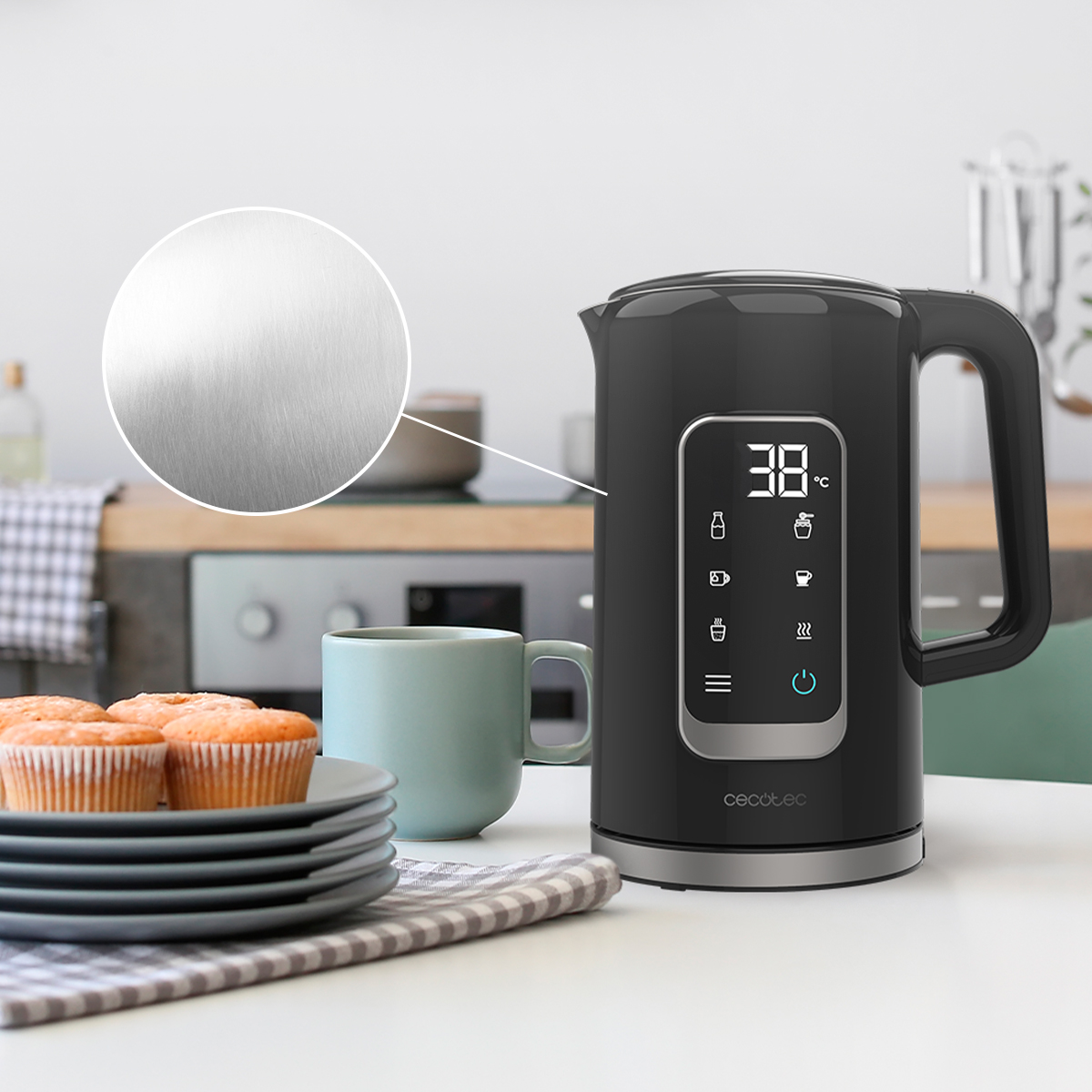 Un hervidor negro con pantalla digital está sobre una mesa al lado de magdalenas y una taza.