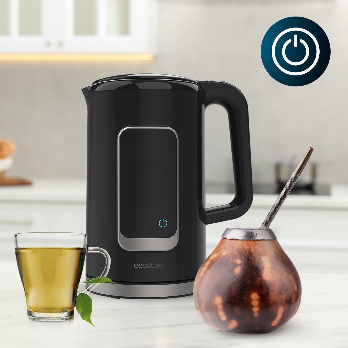 Un hervidor eléctrico negro en un mostrador junto a una taza de té y un mate.