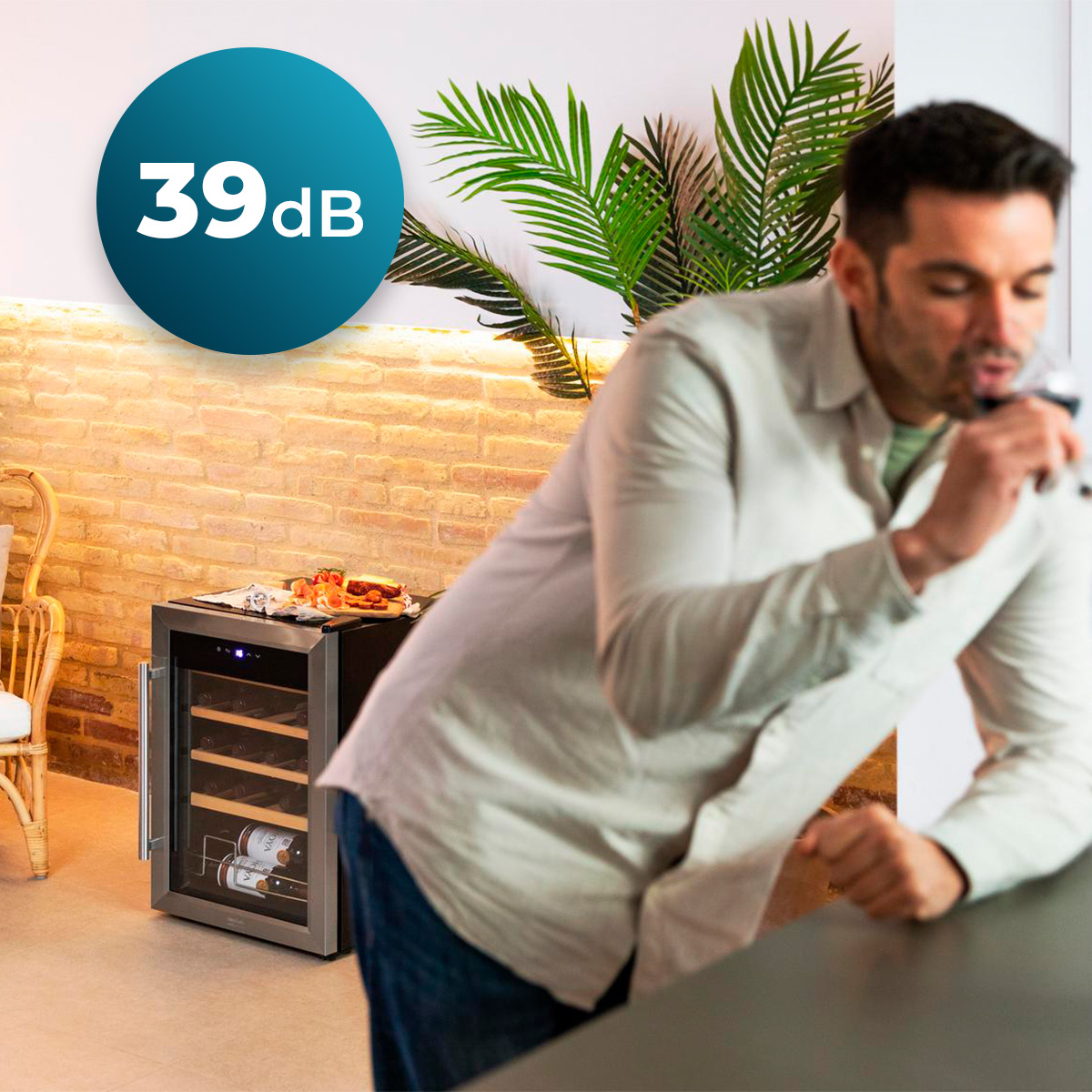 Un uomo beve vino in una cucina moderna con una piccola cantinetta e una parete in mattoni.