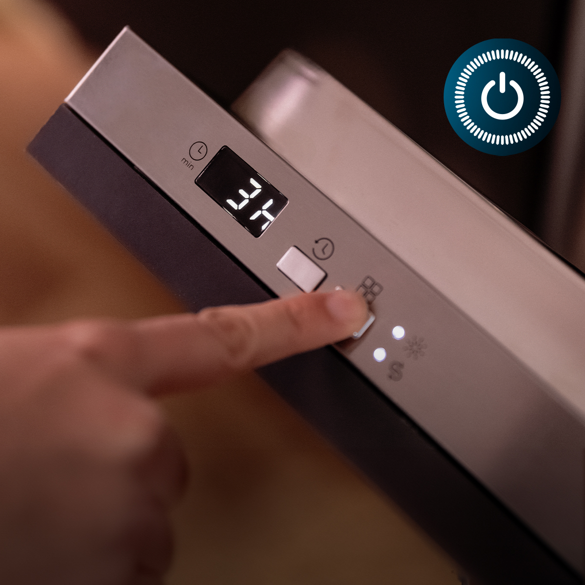 Un dedo presiona un botón en un panel de control de acero inoxidable con pantalla digital que muestra 3H.