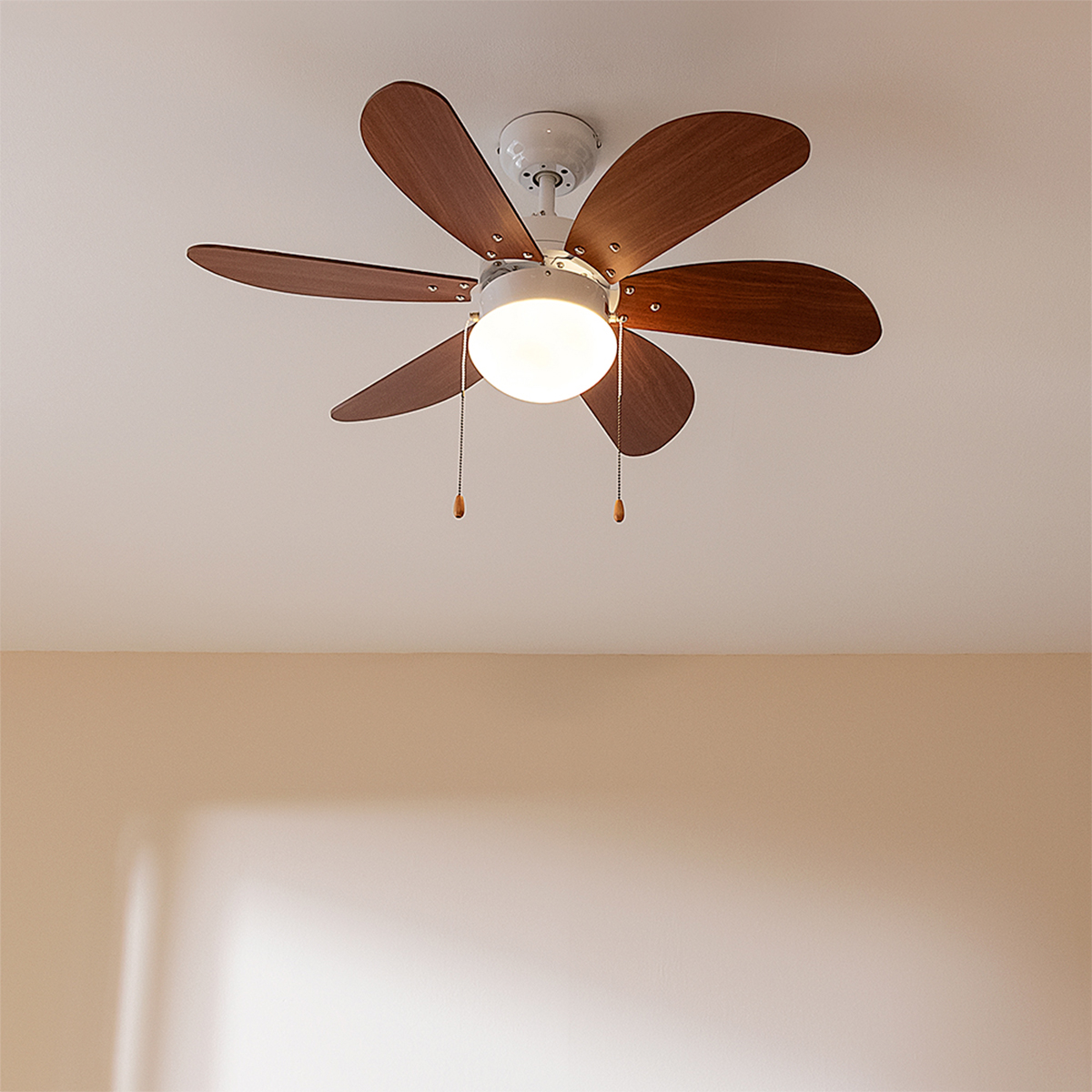 Ein weißer Deckenventilator mit sechs Holzflügeln und einer beleuchteten Lampe in der Mitte hängt an der Decke.