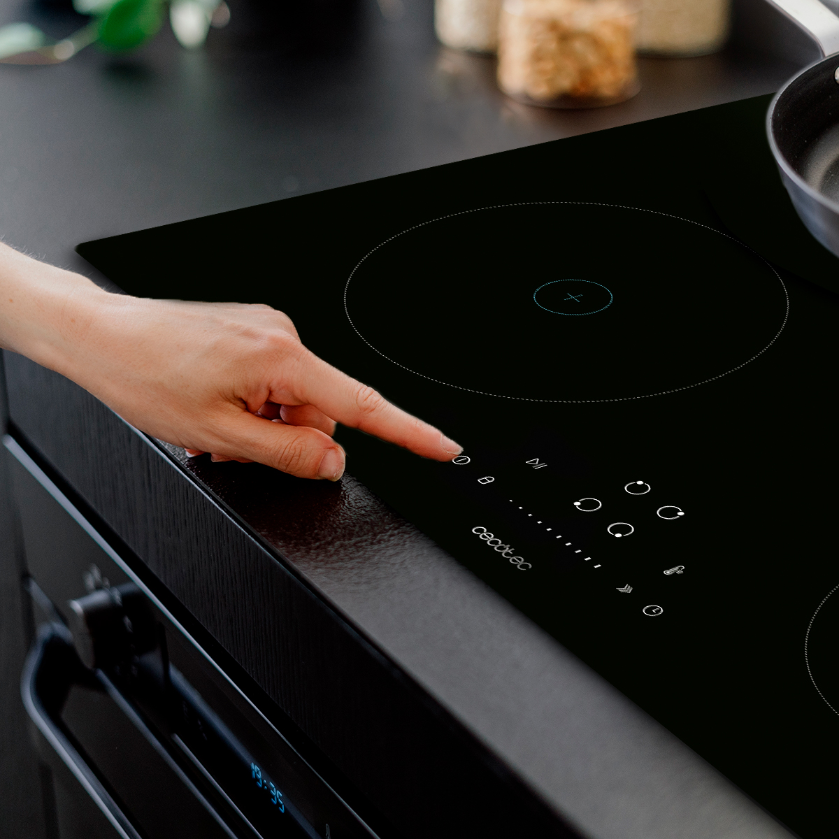 Una mano toca el panel de control táctil de una placa de inducción negra en una cocina moderna.
