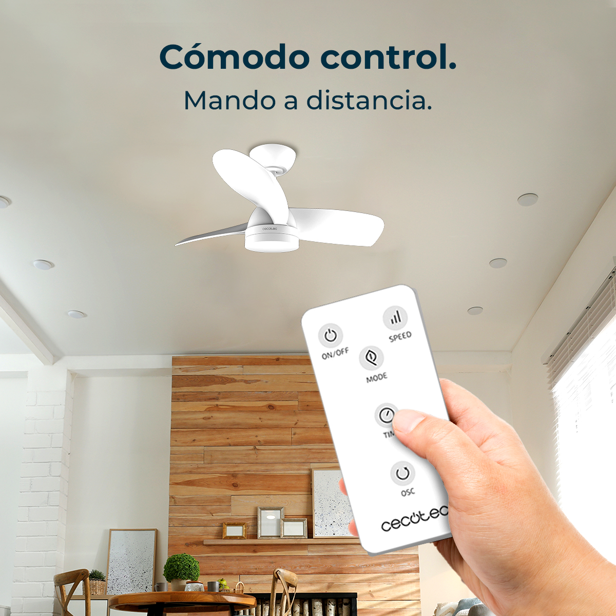 Una mano tiene un telecomando Cecotec bianco davanti a un ventilatore a soffitto in una stanza moderna.