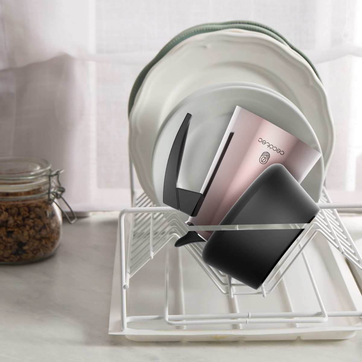 Una cafetera moka rosa colocada en un escurriplatos blanco en la encimera de una cocina.