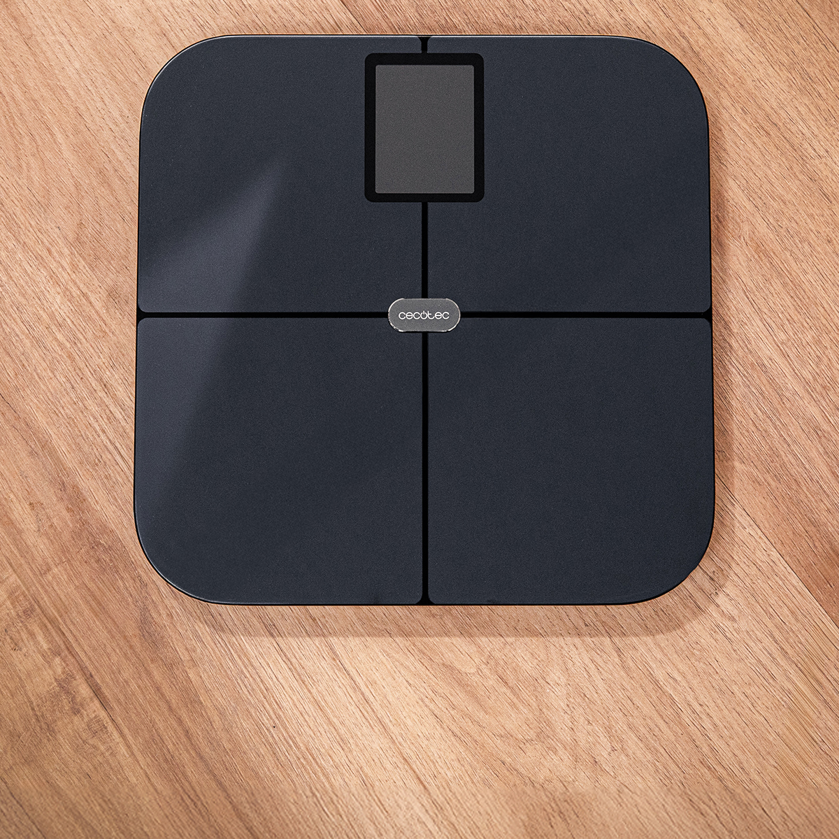 Una bilancia pesapersone digitale nera con logo Cecotec su pavimento in legno.