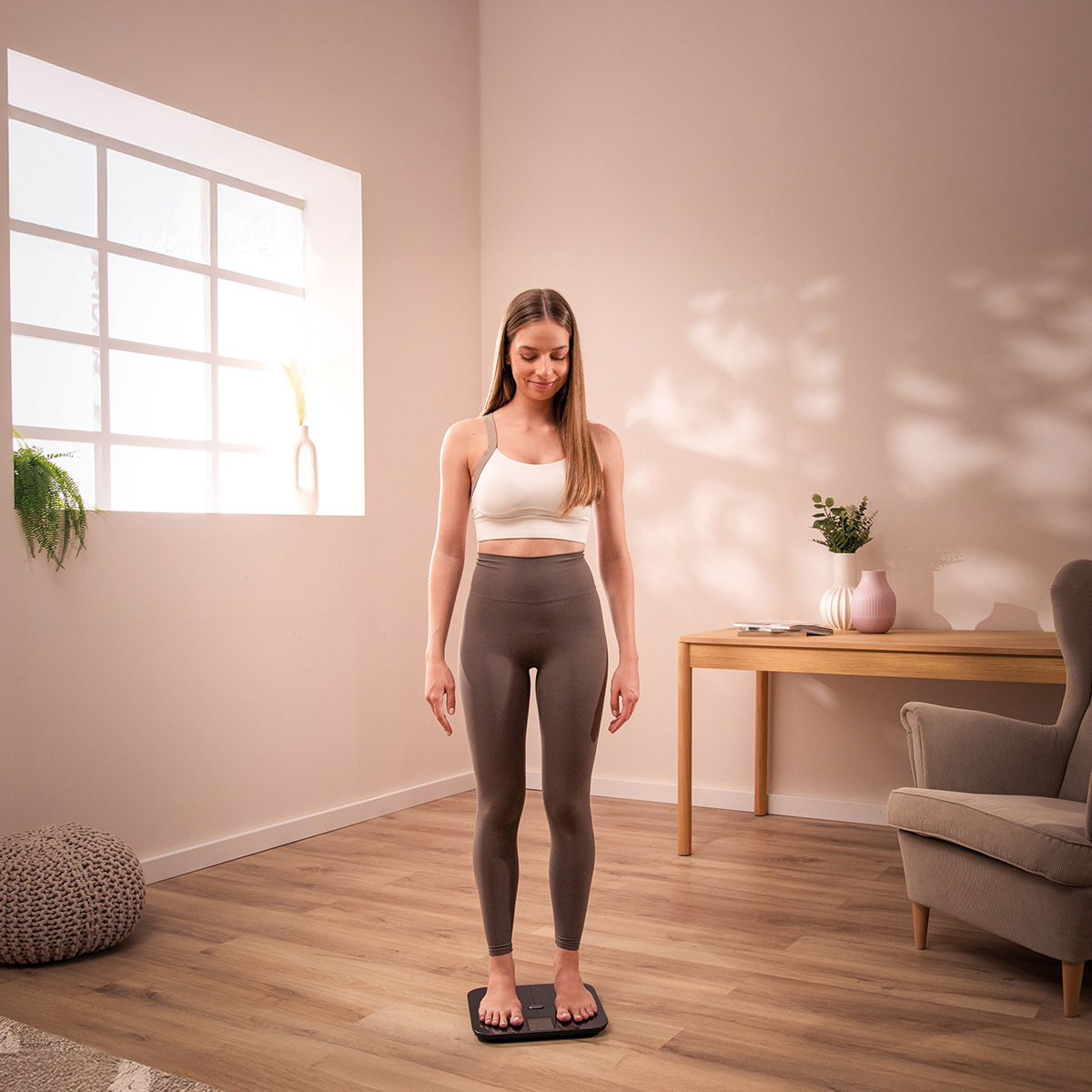 Una donna in abbigliamento sportivo sale su una bilancia digitale in una stanza luminosa.