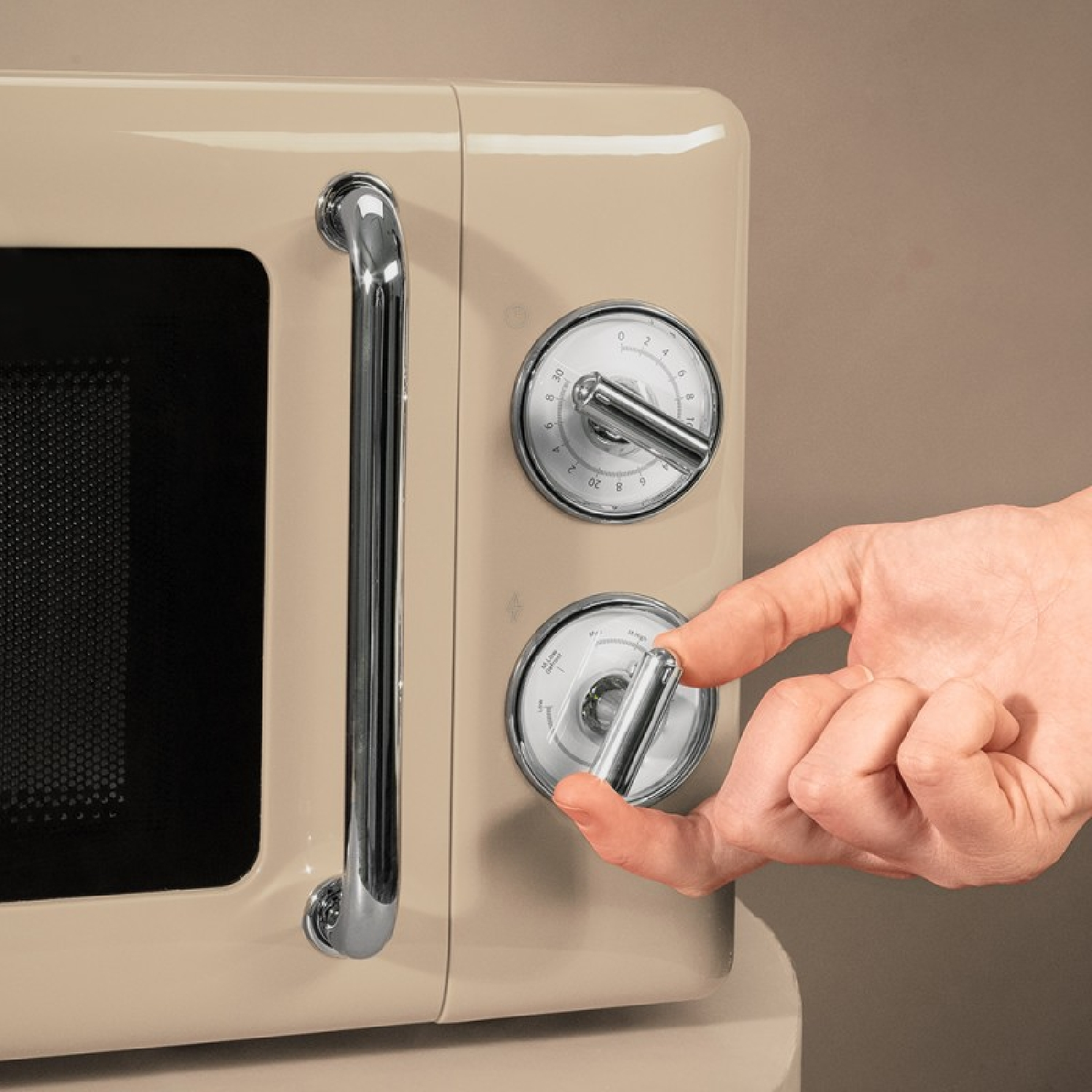Una mano gira la manopola cromata di un forno a microonde retrò beige con maniglia.