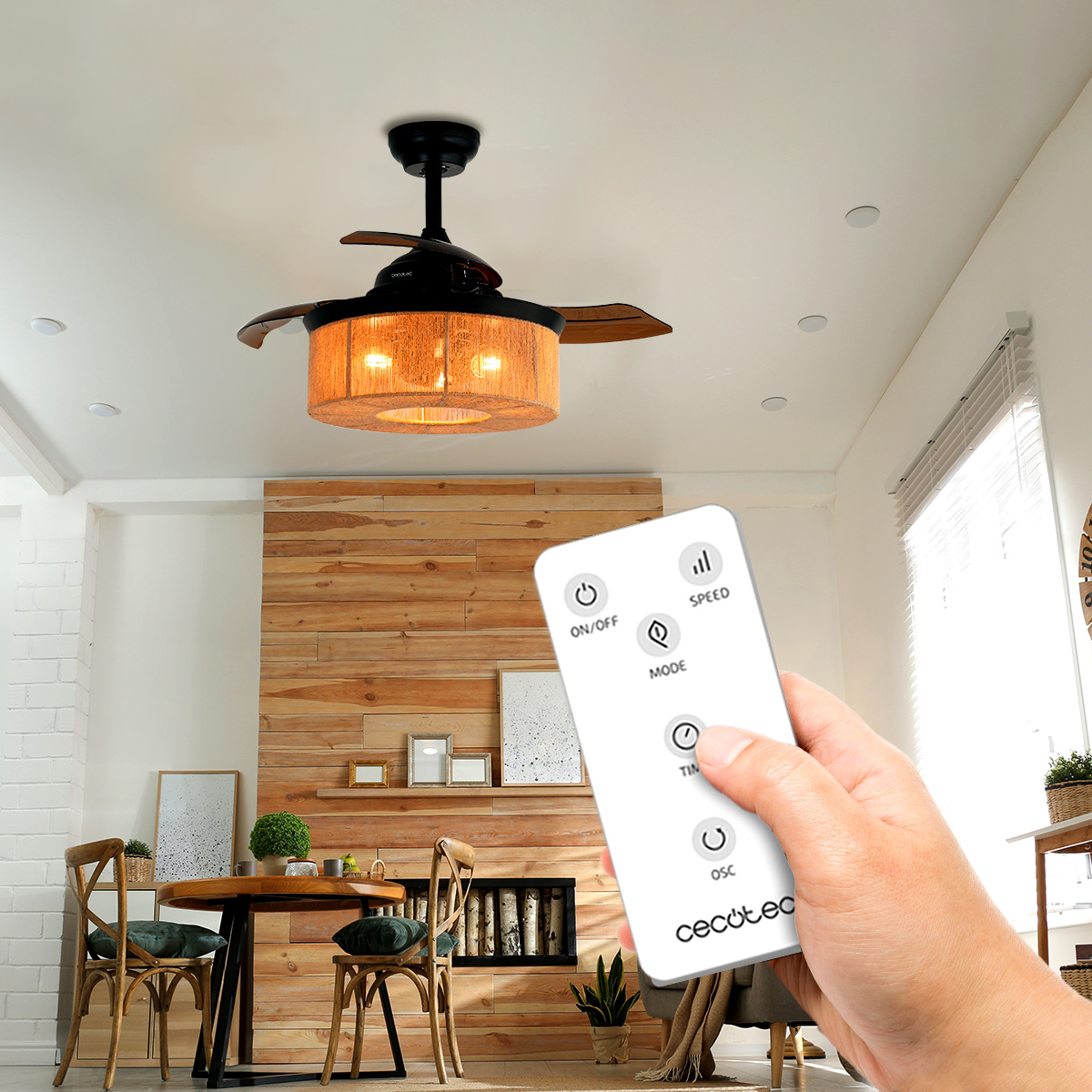 Una mano tiene un telecomando bianco in un soggiorno moderno con ventilatore a soffitto acceso.