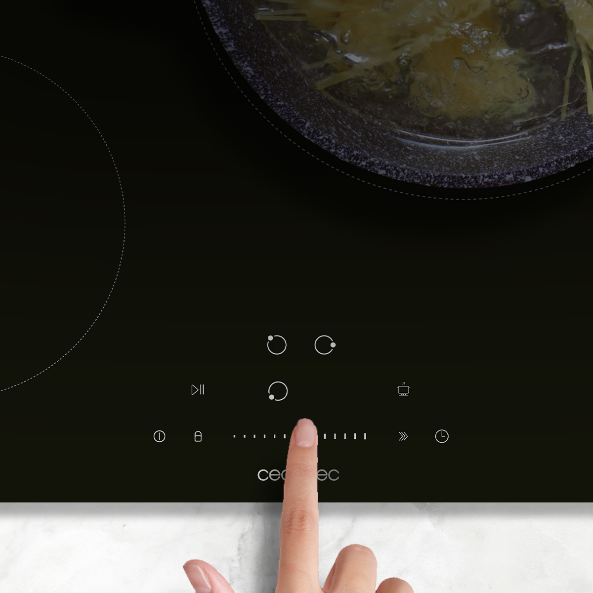 Una mano toca el panel de control táctil de una placa de inducción negra con utensilios de cocina.