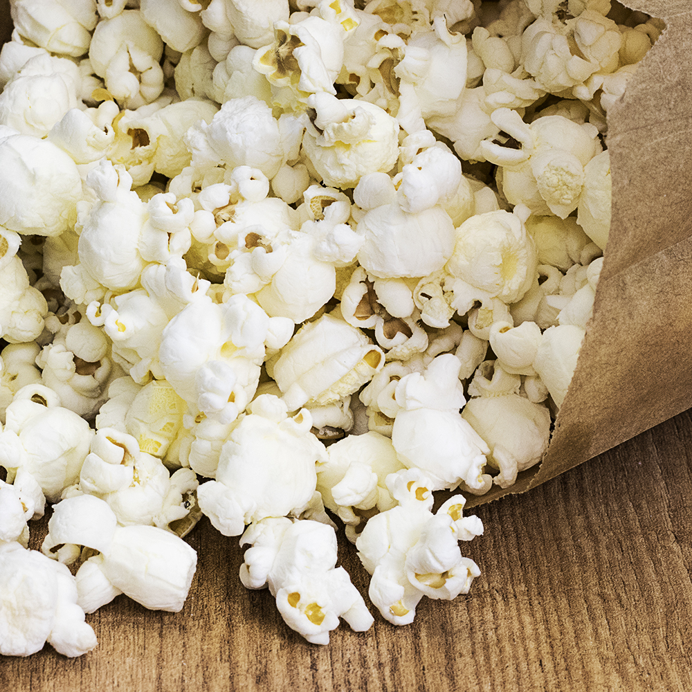 Popcorn fresco fuoriesce da un sacchetto di carta marrone su un tavolo di legno.