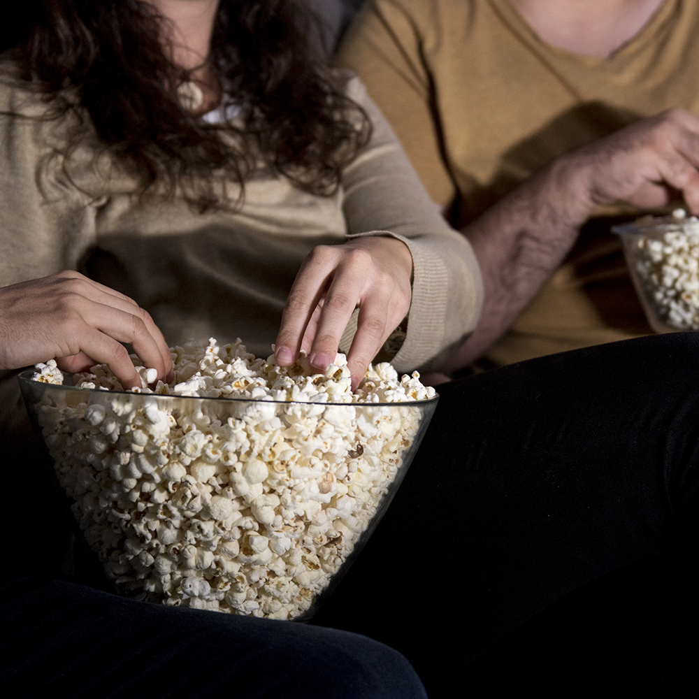 Due persone sedute al cinema che prendono i popcorn da una ciotola grande.