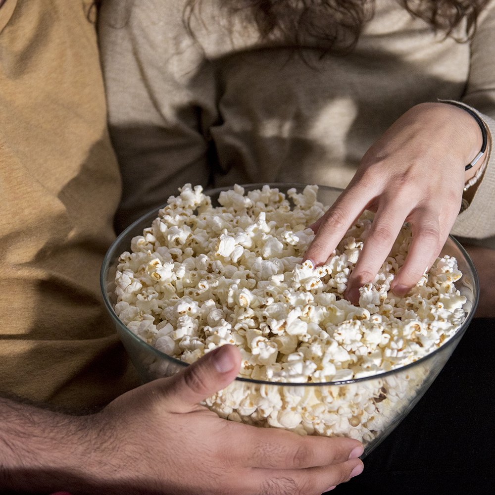 Due persone tengono insieme una grande ciotola di vetro piena di popcorn.
