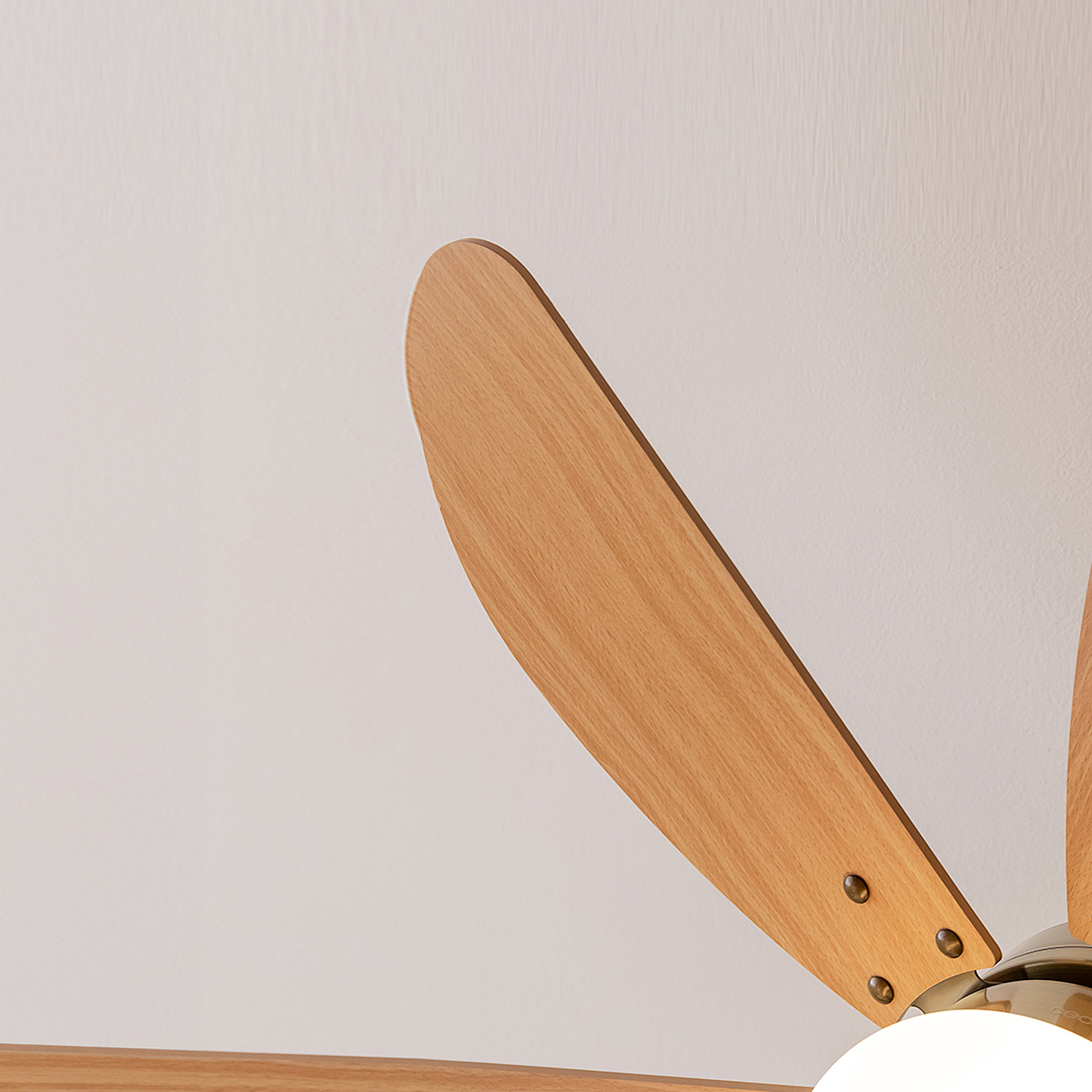 Pale di ventilatore color legno con viti in ottone su parete bianca.