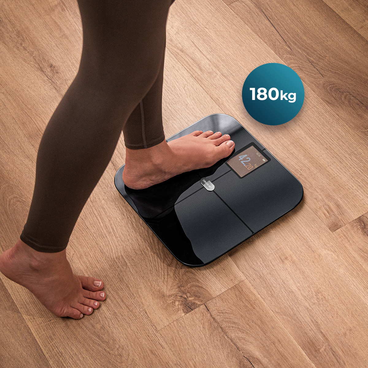 Una persona in piedi a piedi nudi su una moderna bilancia digitale nera su pavimento in legno.