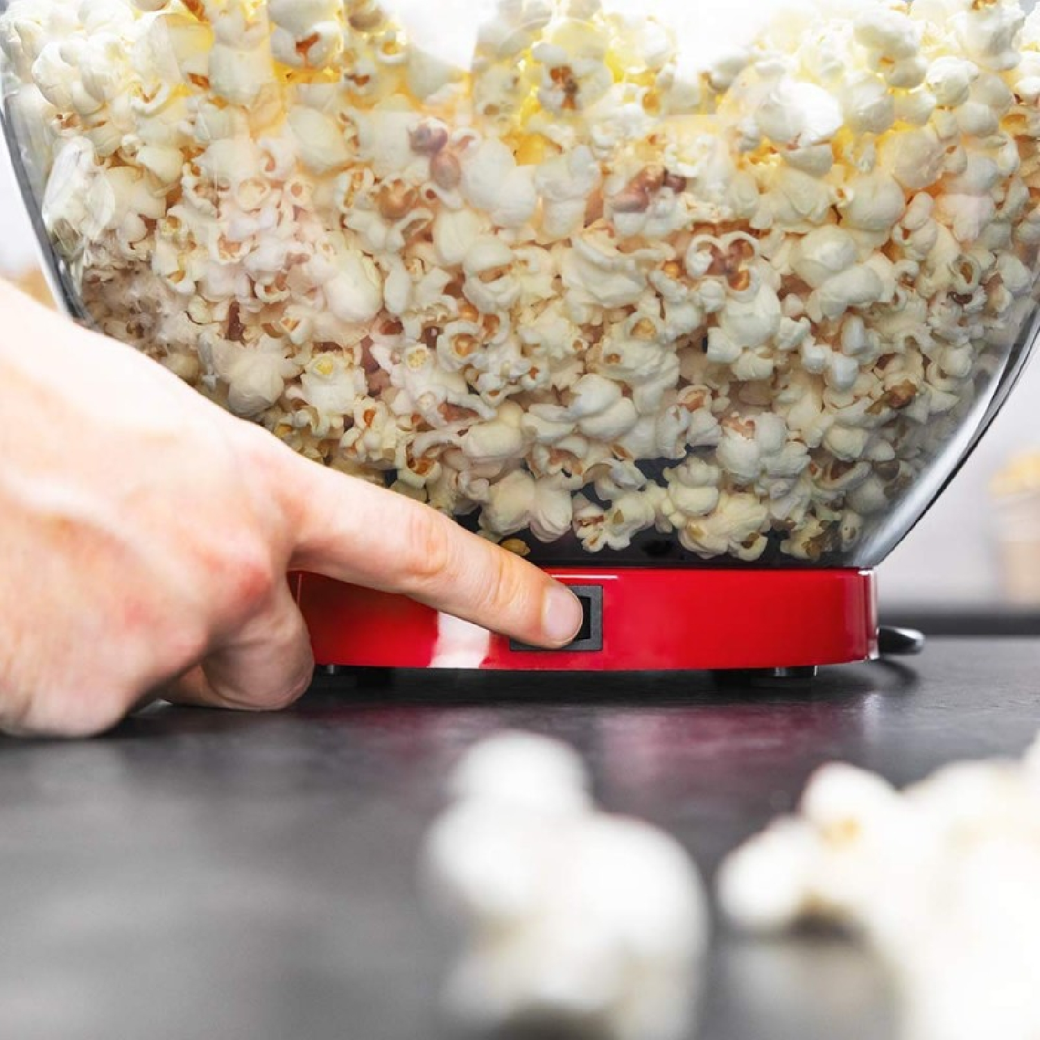 Una mano presiona el interruptor de una máquina de palomitas roja llena de palomitas.