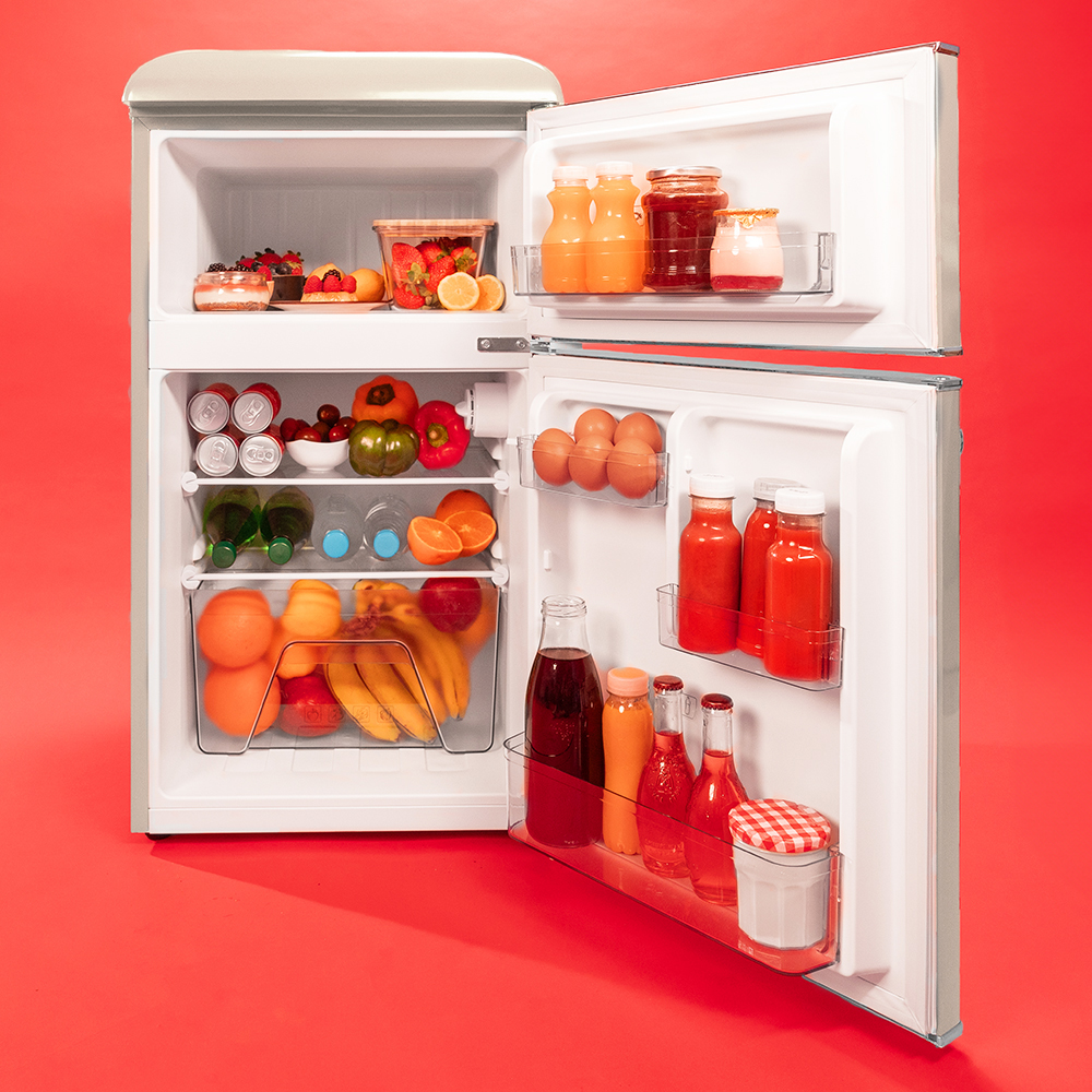Un refrigerador abierto lleno de frutas coloridas, bebidas y alimentos sobre un fondo rojo.