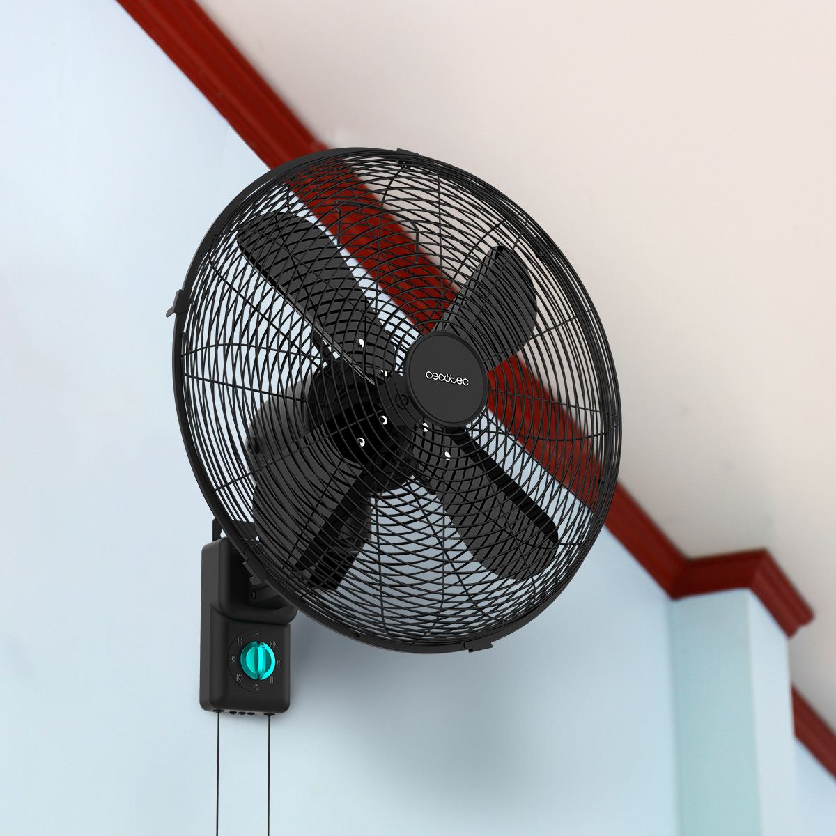 Un ventilador de pared negro con rejilla protectora y un mando turquesa montado en una pared azul claro.