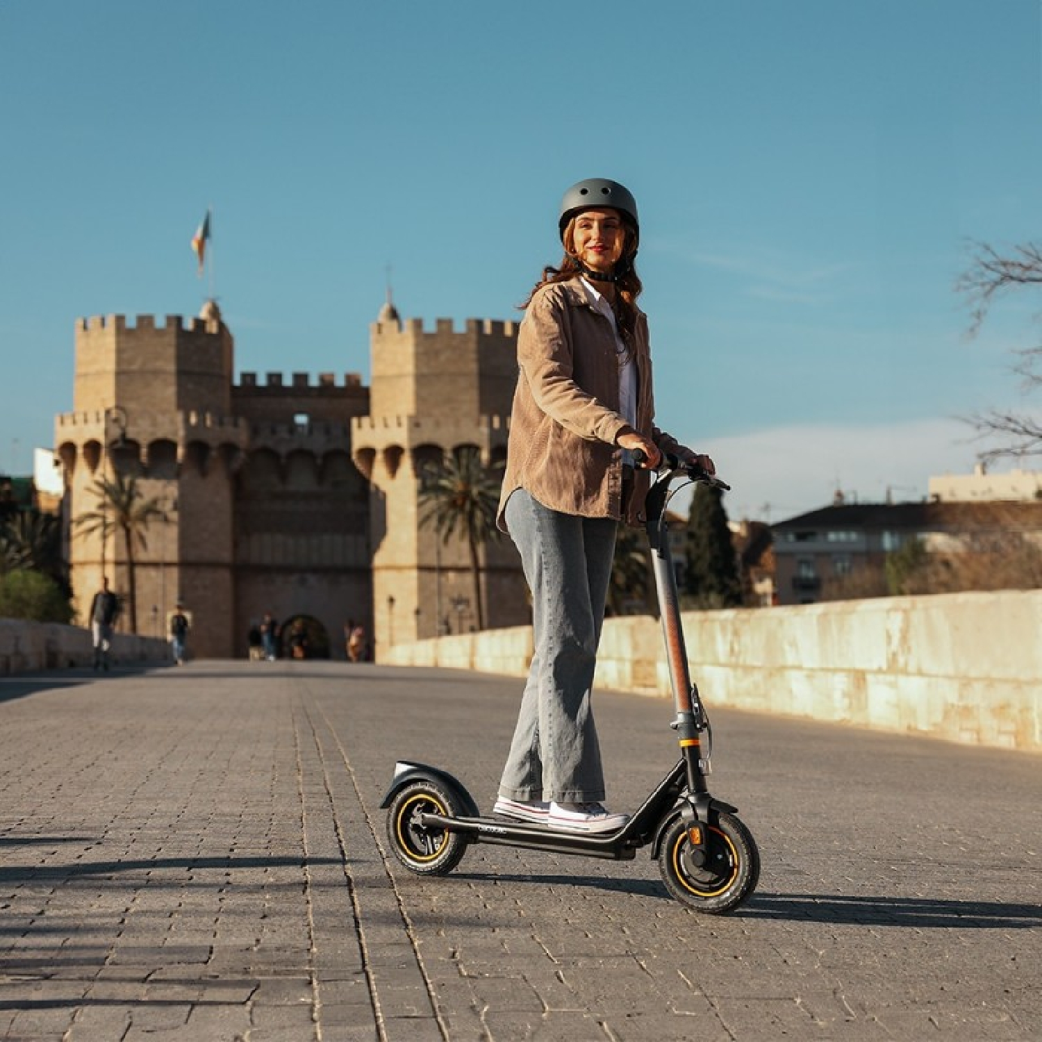 Una donna con casco guida un monopattino elettrico davanti a un castello storico.