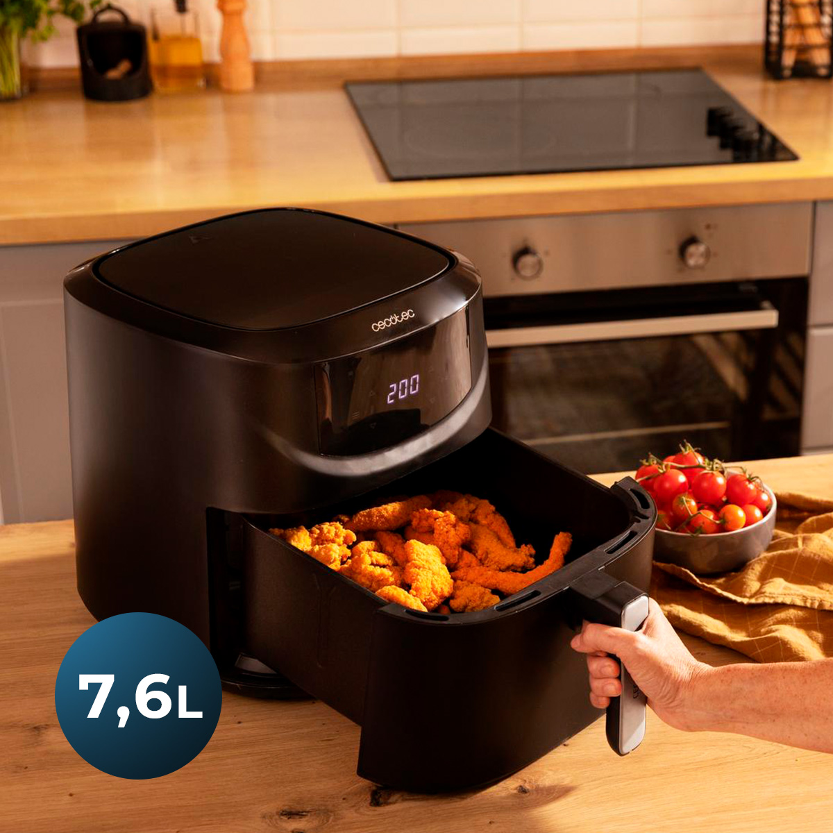 Friggitrice ad aria nera con cassetto estratto pieno di pollo fritto su un tavolo da cucina in legno.
