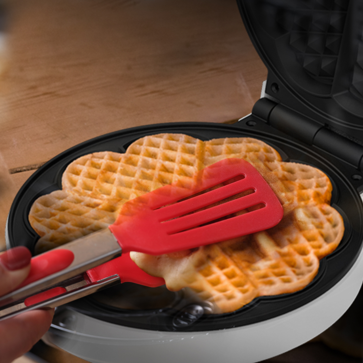 Una mano usa delle pinze rosse per rimuovere dei waffle appena sfornati da una piastra.