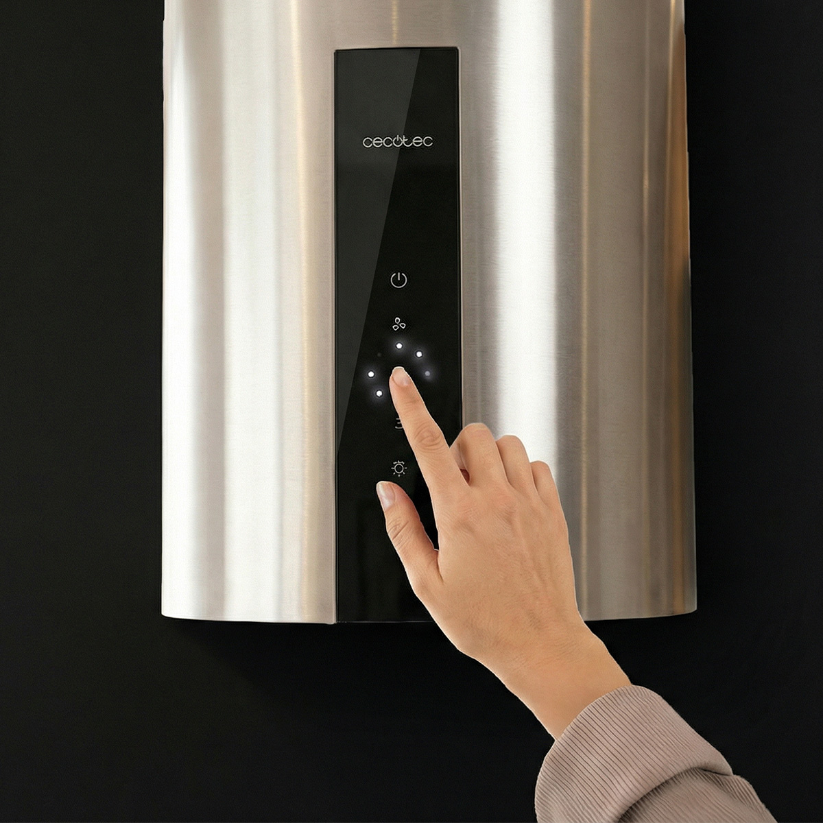 Una mano tocando el panel de control táctil iluminado de una campana extractora de acero inoxidable.