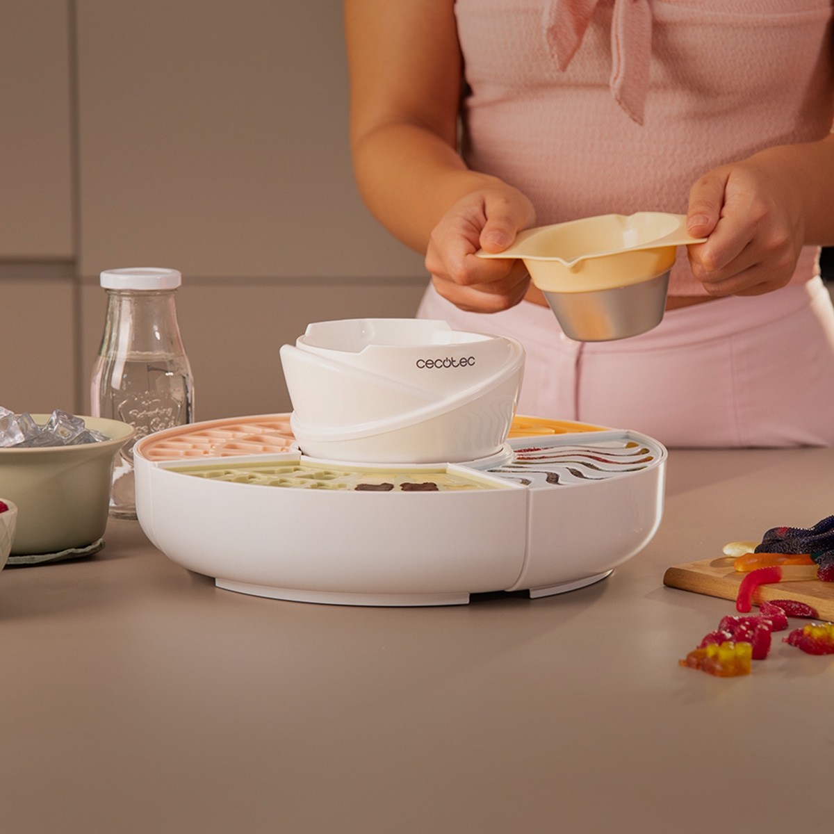Una persona de rosa sostiene un bol pequeño sobre una heladera blanca Cecotec con ingredientes.