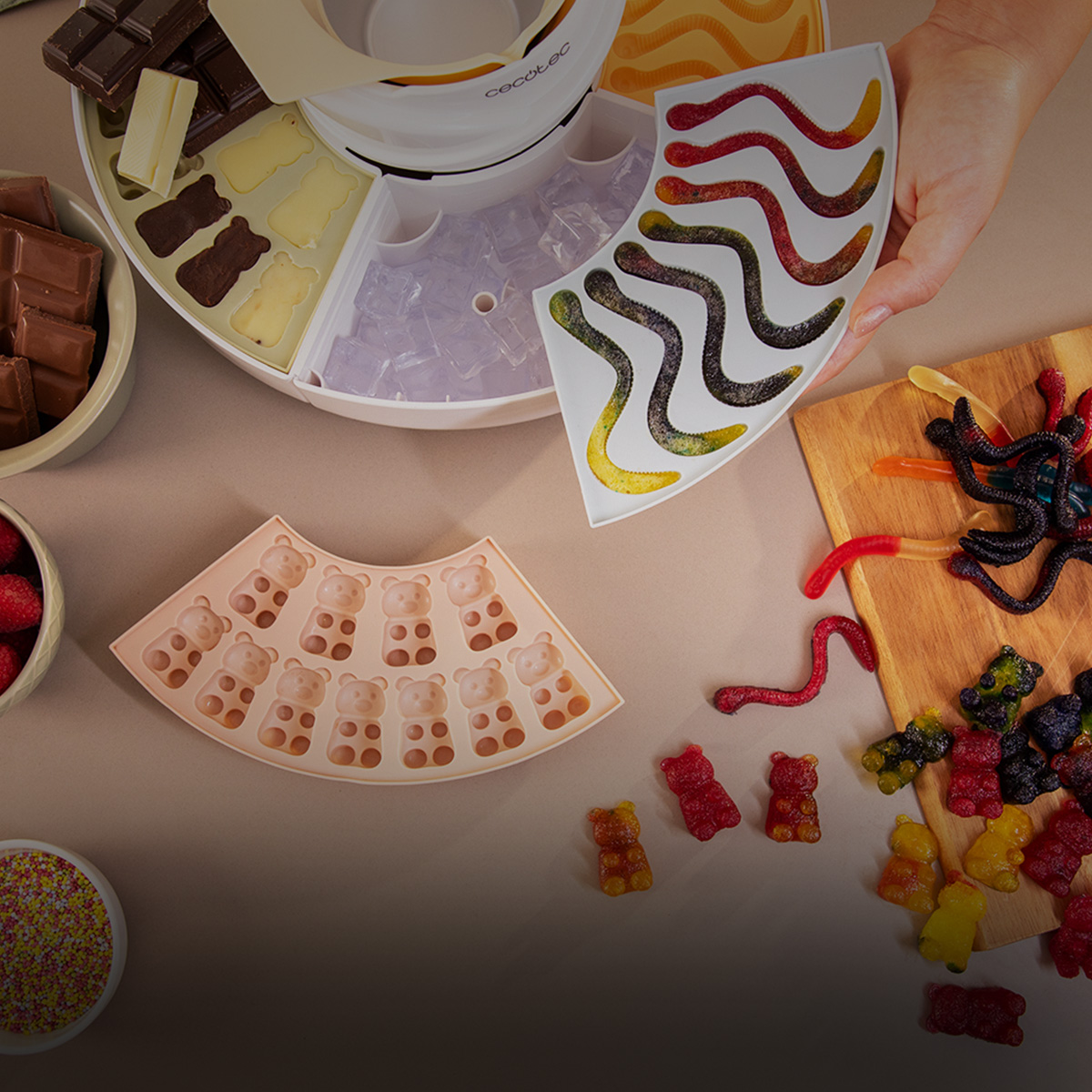 Elaboración de gominolas y chocolate con moldes, bayas y chocolate derretido sobre una mesa.