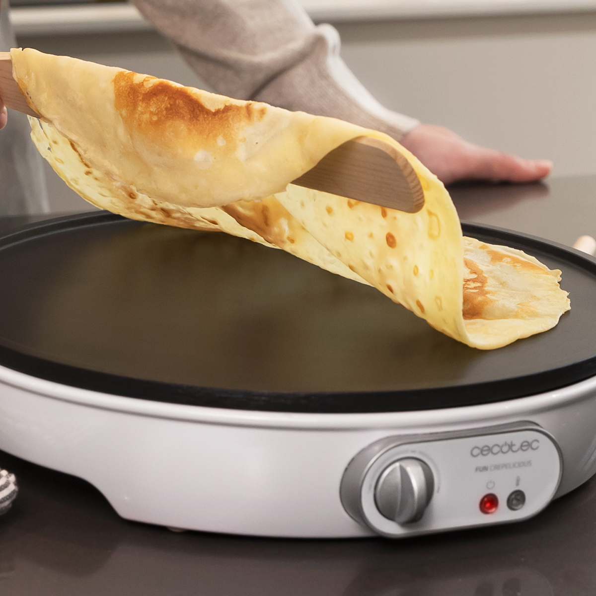 Una mano usa una spatola di legno per girare una crepe su una piastra elettrica.