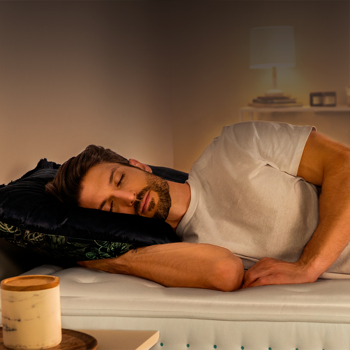 Un joven duerme plácidamente sobre una almohada en un colchón suave en una habitación con poca luz.