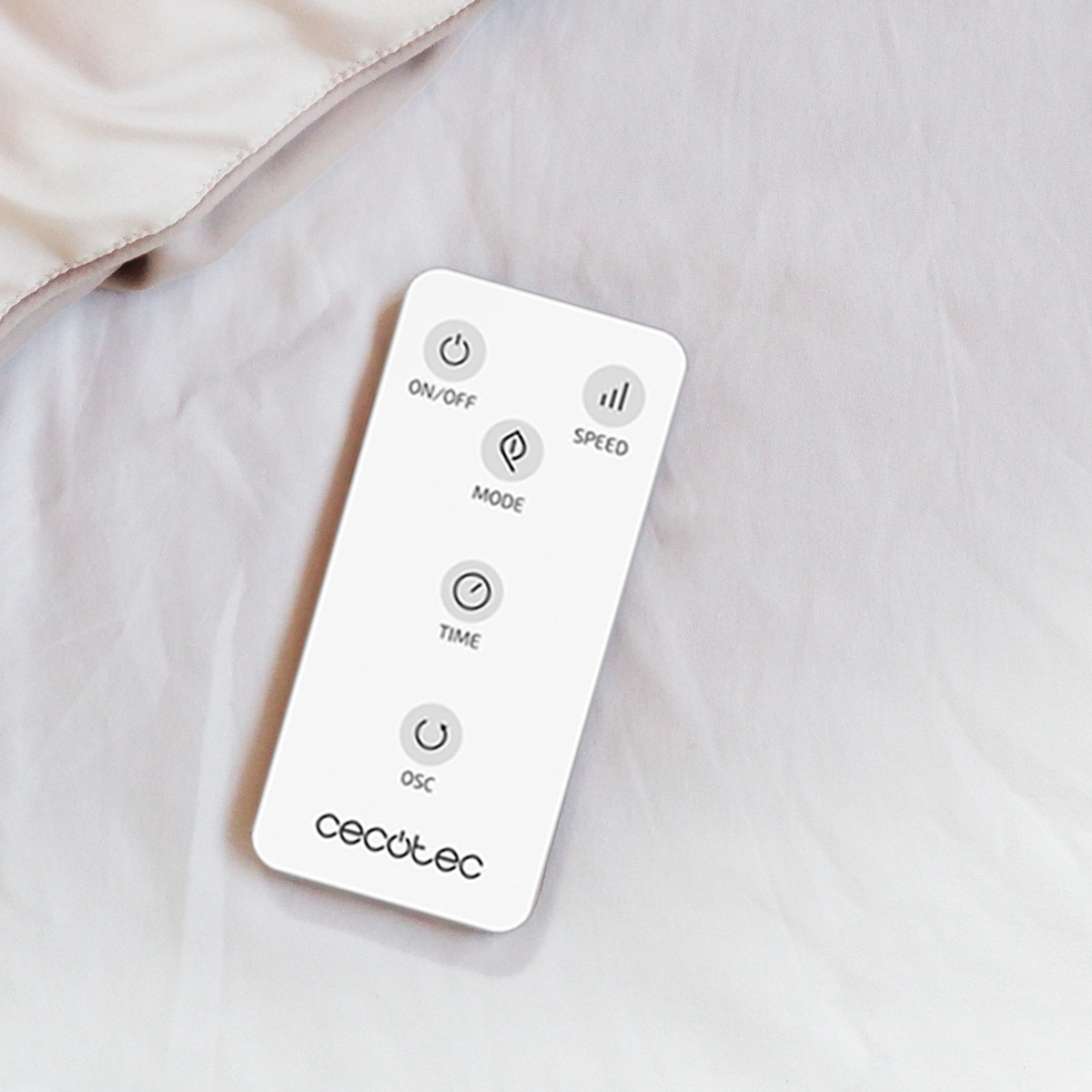 Un control remoto blanco de Cecotec con cinco botones sobre una sábana clara.