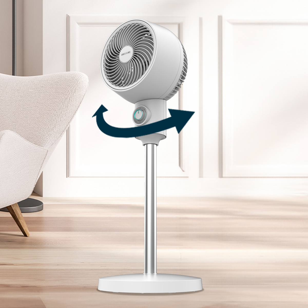 Un ventilador de pie blanco en una habitación con sillón y suelo de madera. Flechas azules indican oscilación.