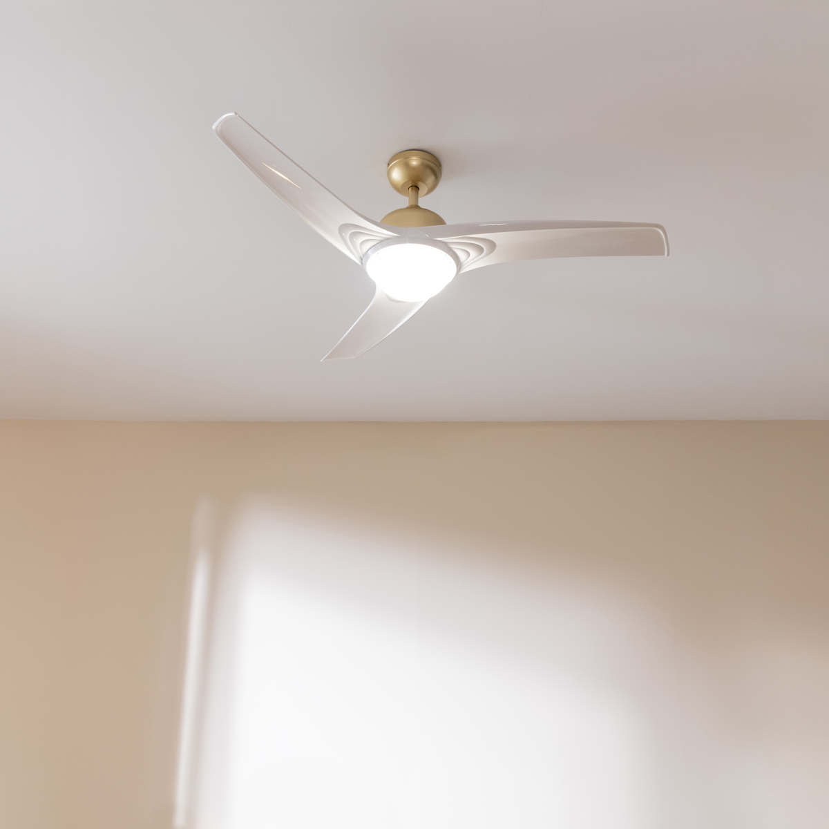 Un moderno ventilatore da soffitto bianco con supporto dorato e luce centrale su un soffitto bianco.