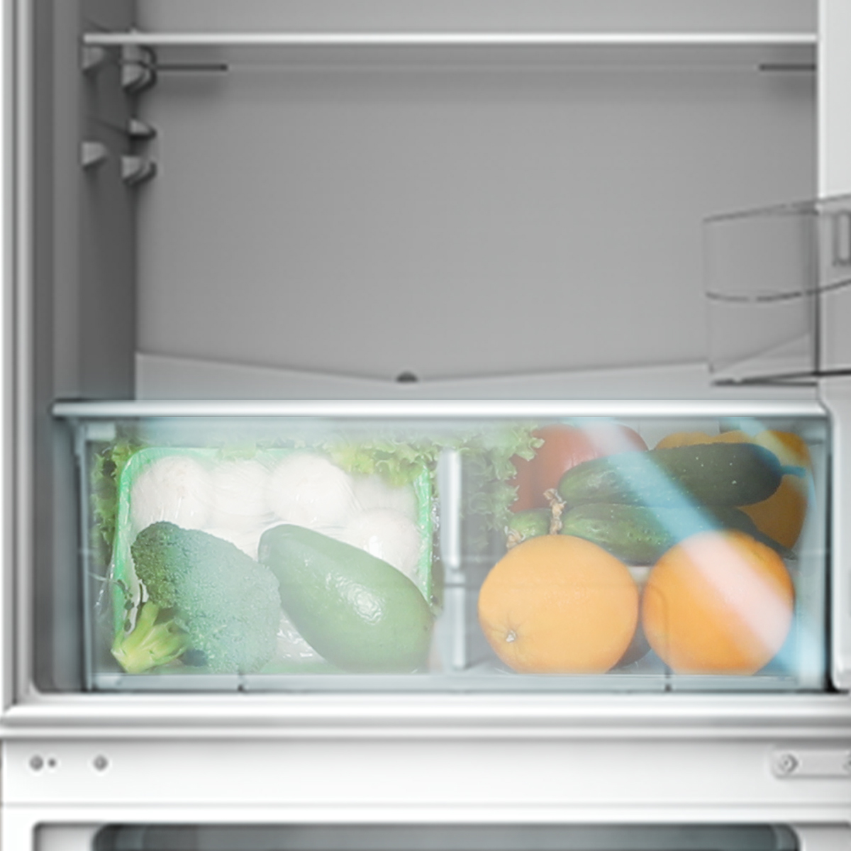 Un refrigerador blanco con verduras y frutas frescas en el cajón inferior transparente.
