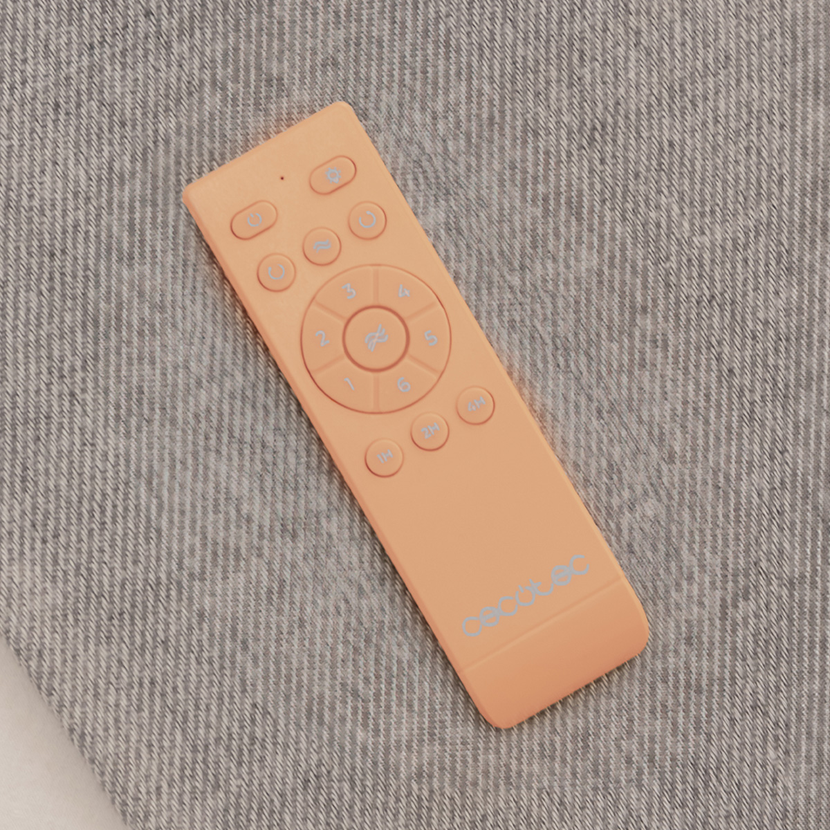 Un telecomando Cecotec arancione con numerosi pulsanti poggia su una superficie di tessuto grigio.