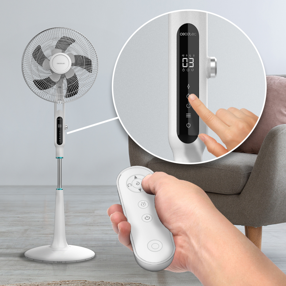 Ventilador de pie blanco con pantalla digital y mando a distancia, junto a un sillón gris.