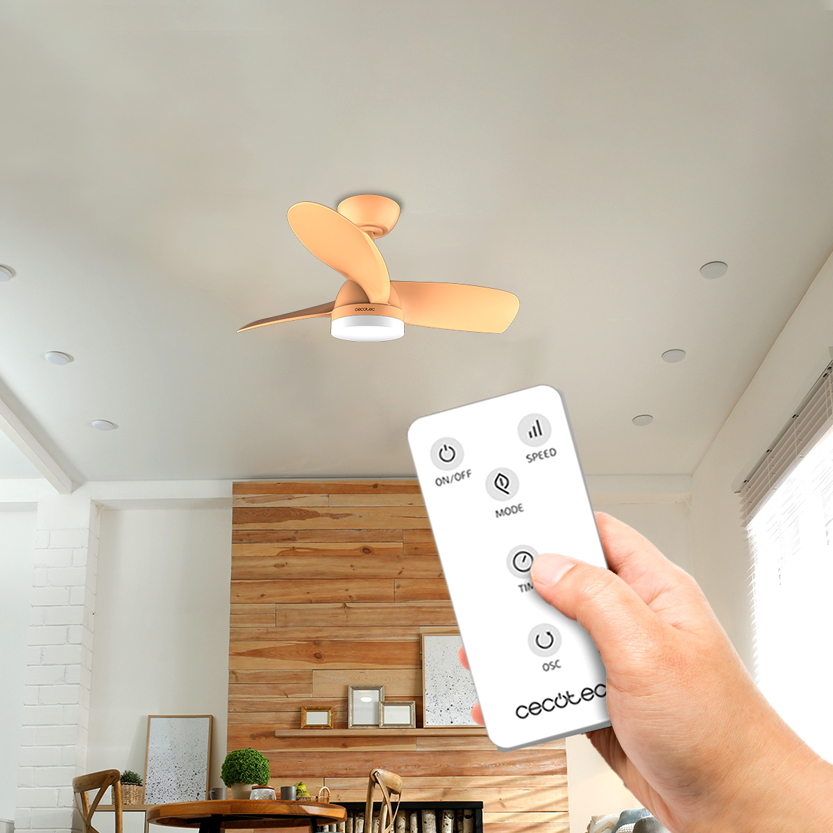 Mano che tiene un telecomando bianco per azionare un ventilatore da soffitto in un soggiorno moderno.