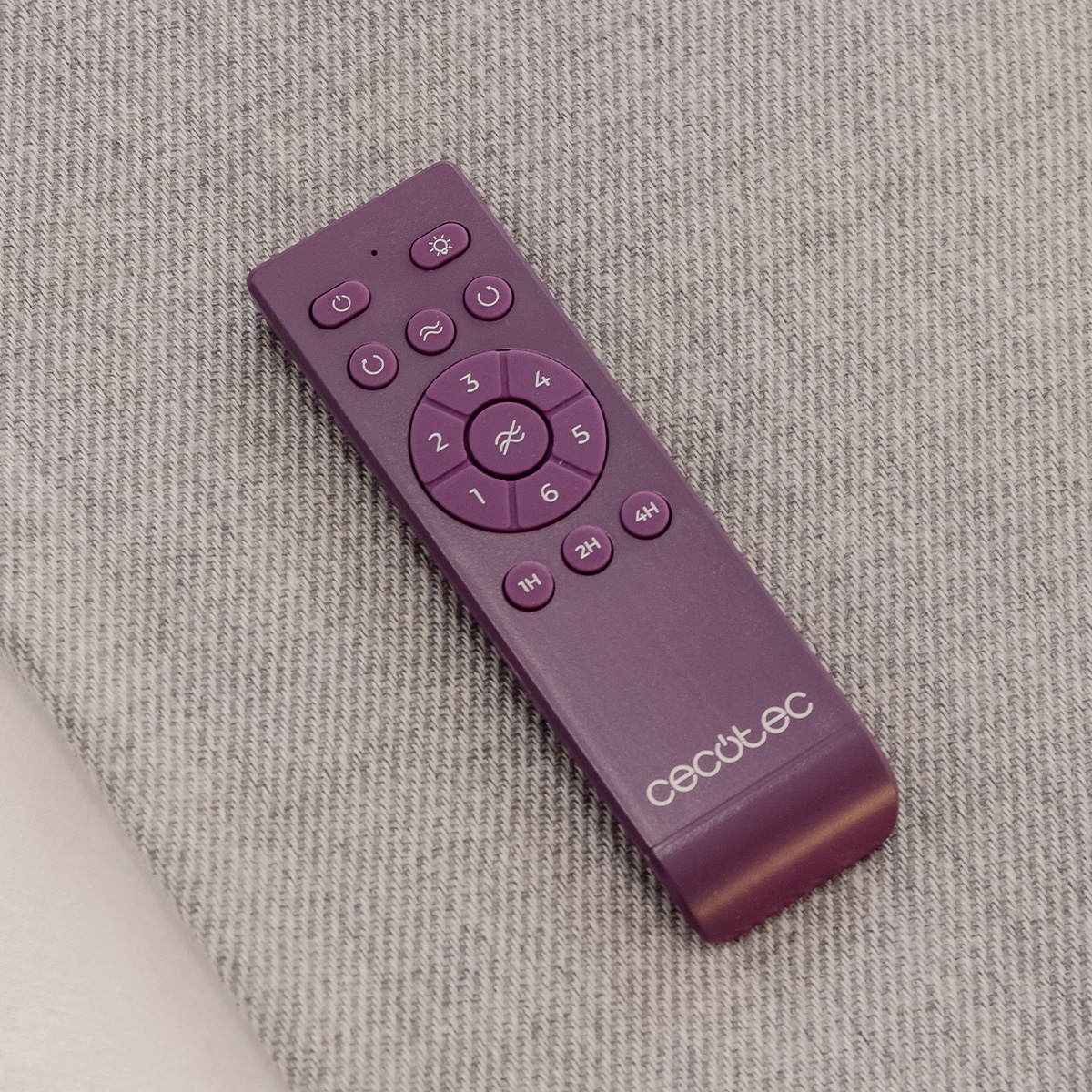 Un telecomando Cecotec viola si trova diagonalmente su un tessuto grigio.
