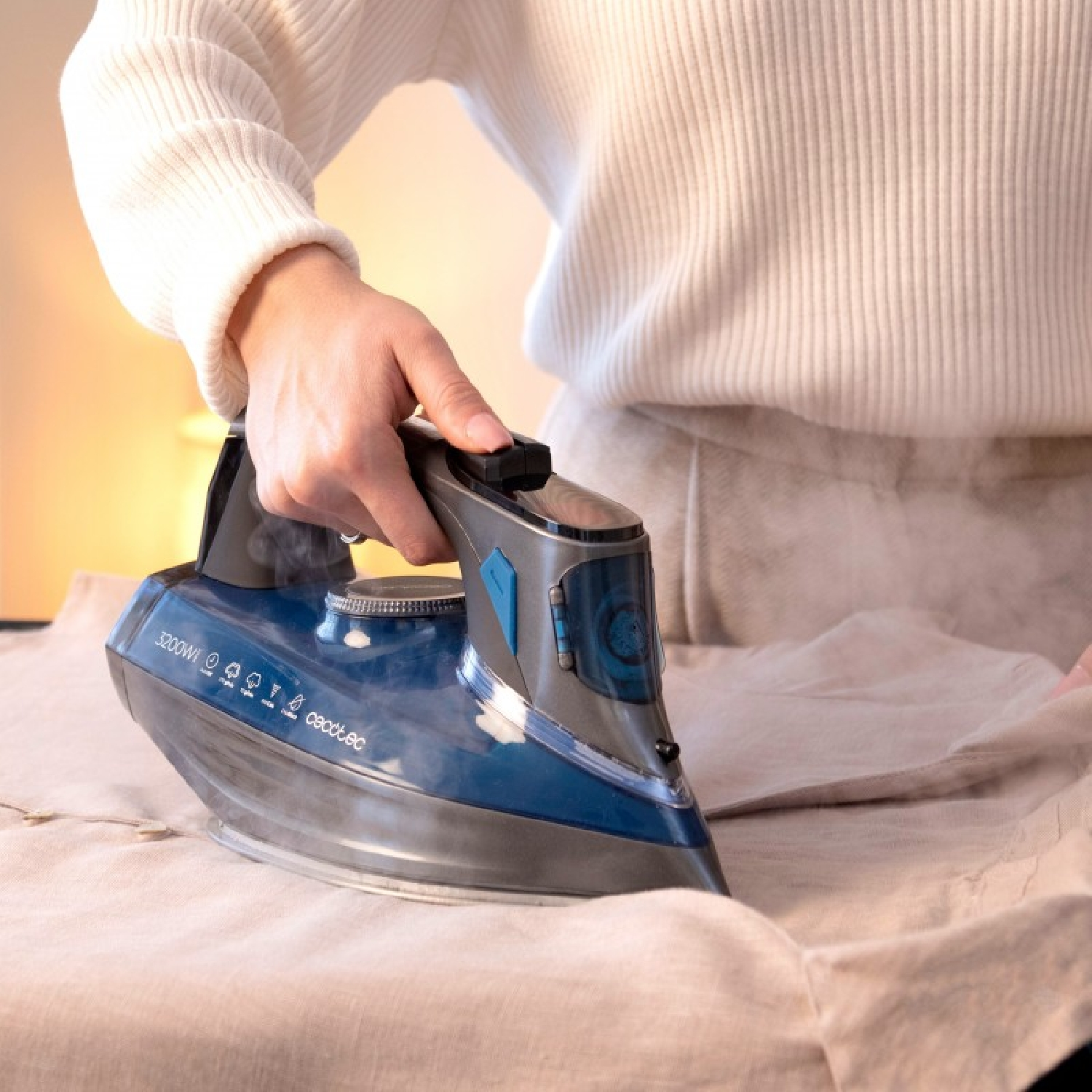 Una persona con maglione bianco usa un ferro da stiro a vapore blu scuro e grigio.