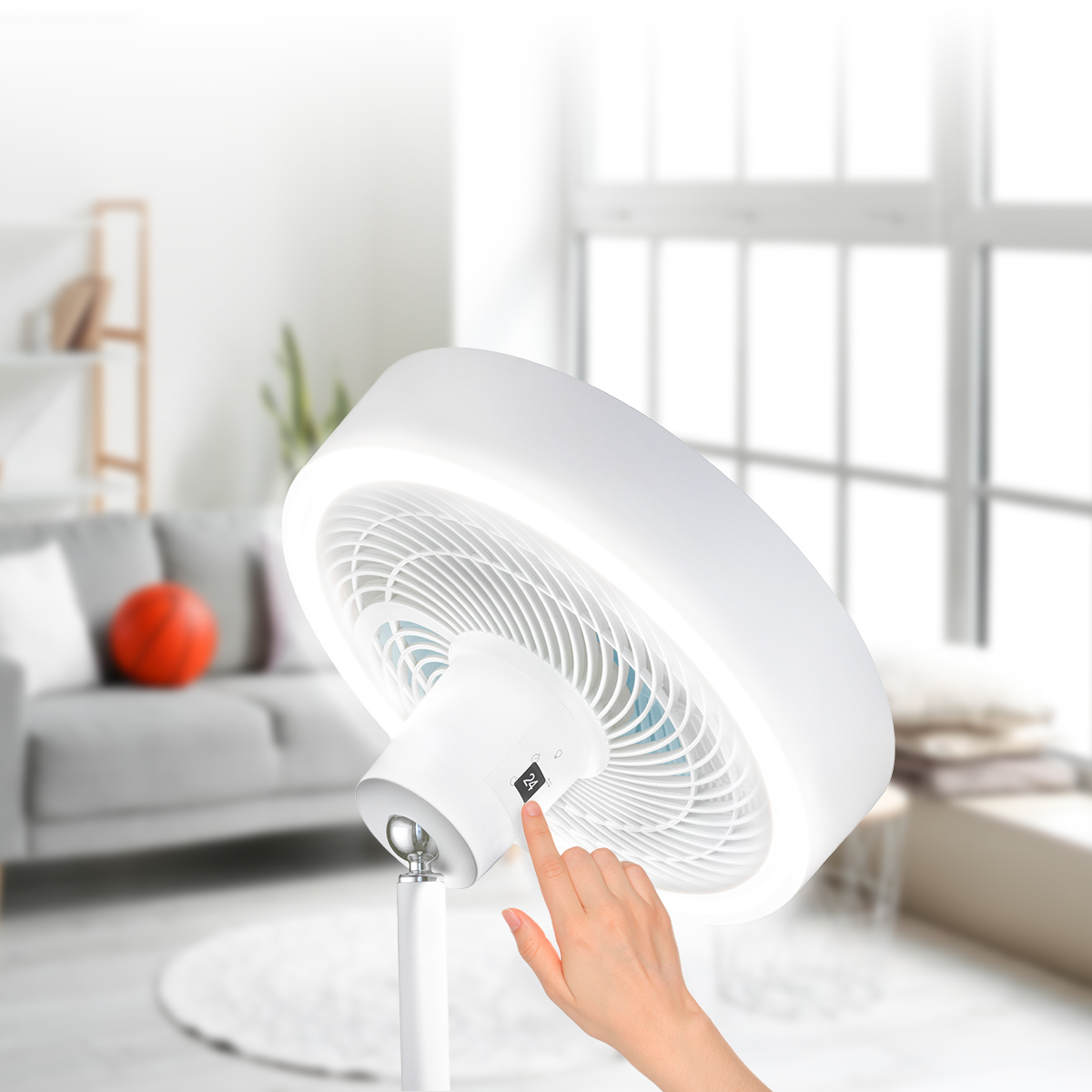 Una mano tocca il pannello di controllo digitale di un ventilatore a piantana bianco in una stanza luminosa.