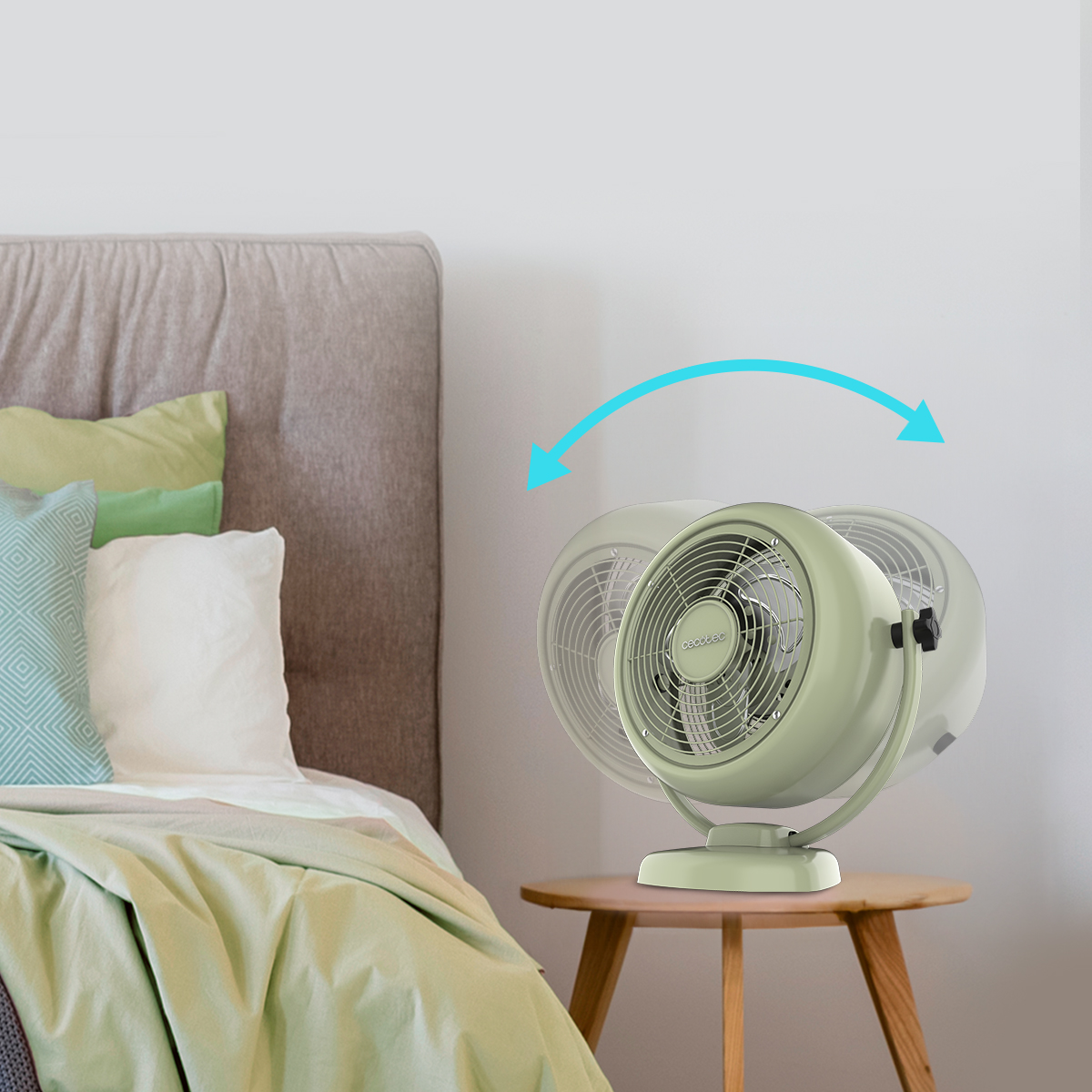 Un ventilatore da tavolo oscillante verde chiaro su un comodino in legno accanto a un letto.