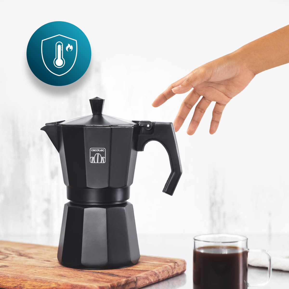 Mano alcanza cafetera moka negra en tabla de madera junto a taza.
