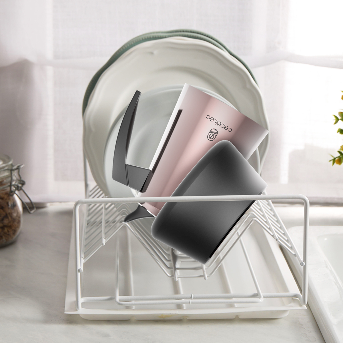Una caffettiera rosa e una tazza nera si trovano su uno scolapiatti bianco.