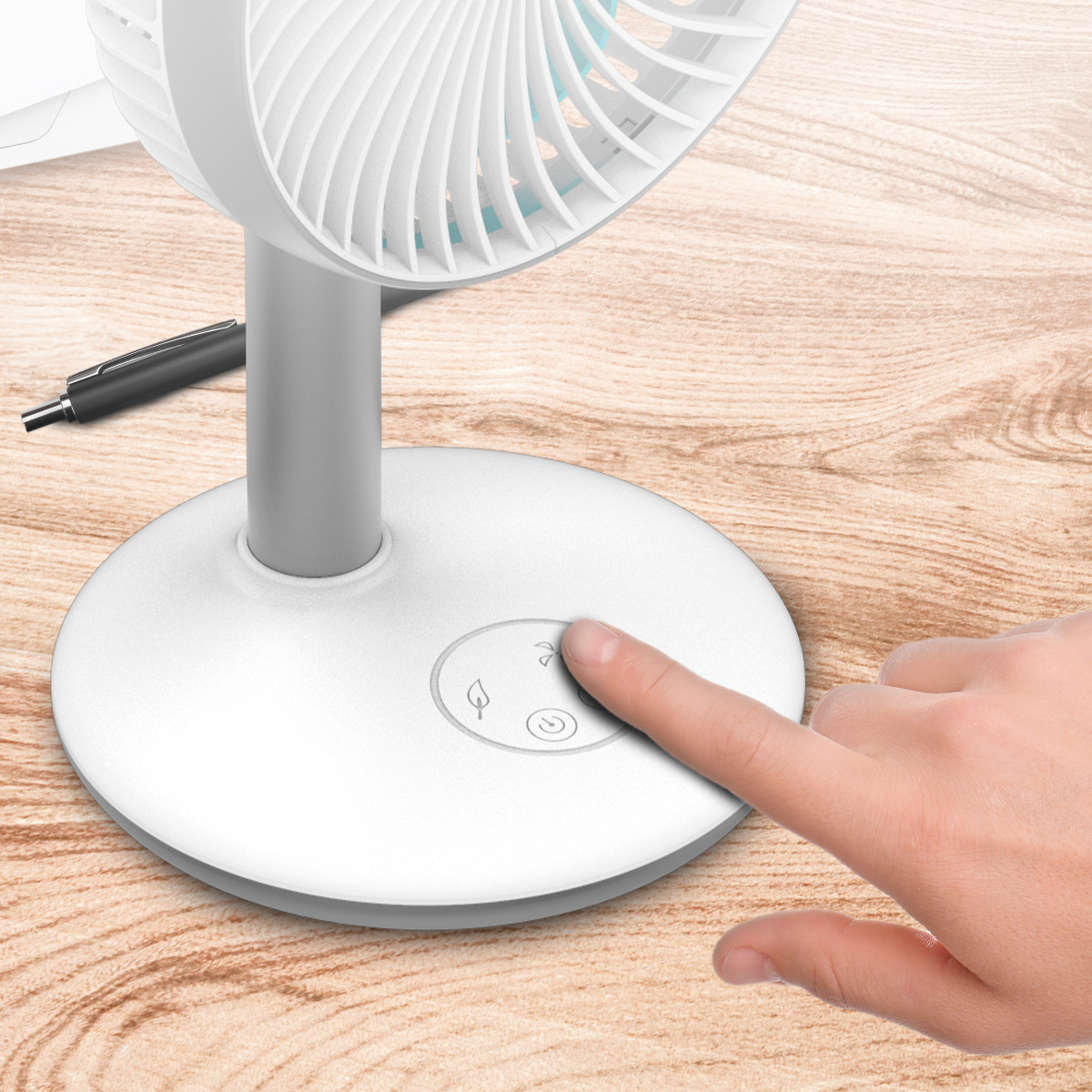 Una mano che tocca il pulsante di accensione di un ventilatore bianco su un tavolo.