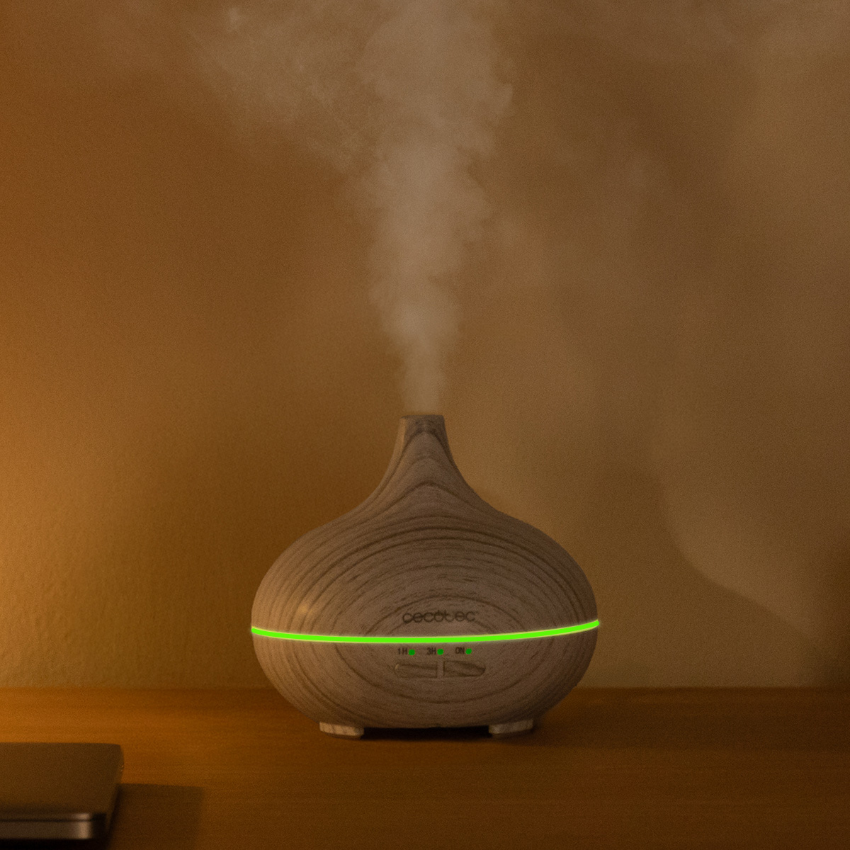 Ein hölzernen Aromadiffusor auf einem Tisch stößt feinen Nebel und ein grünes Licht aus.